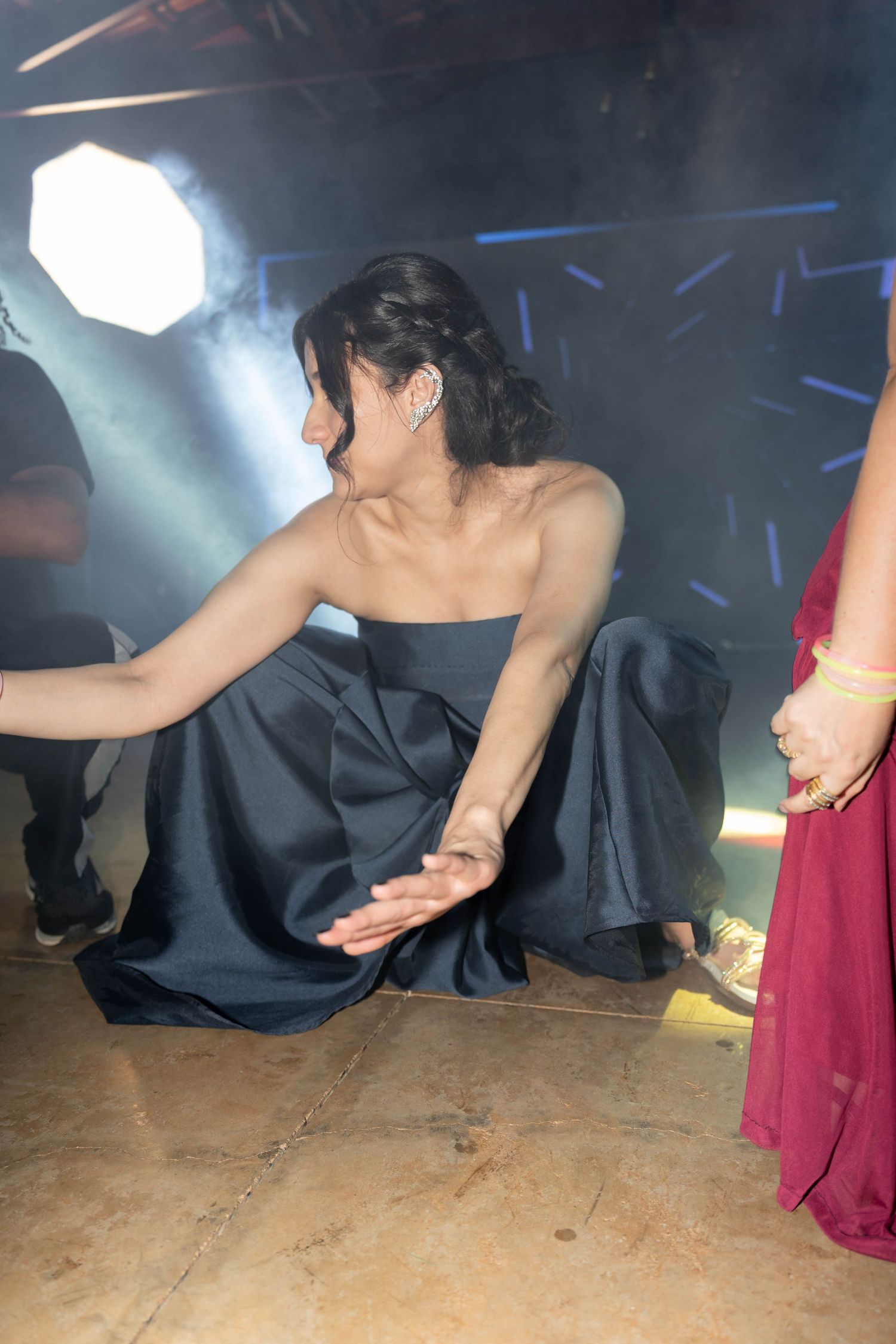 Woman in strapless navy gown crouching gracefully on dance floor with dramatic stage lighting and smoke effects.