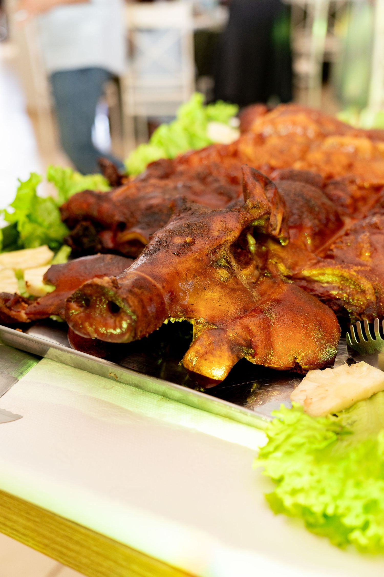 Roasted pig heads garnished with fresh green lettuce leaves served on a metal tray at a buffet.