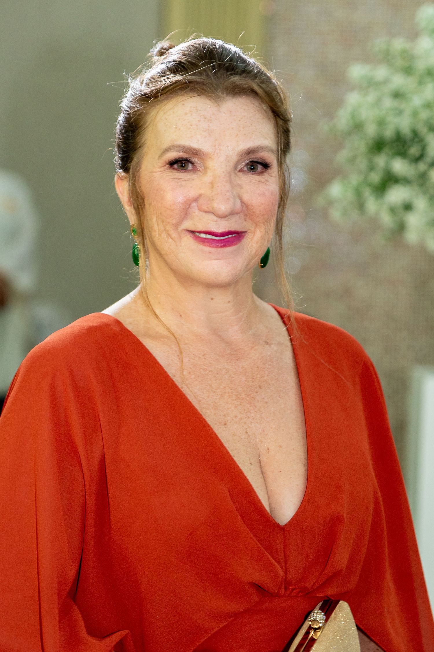 Woman in red dress with green earrings smiling at formal event.