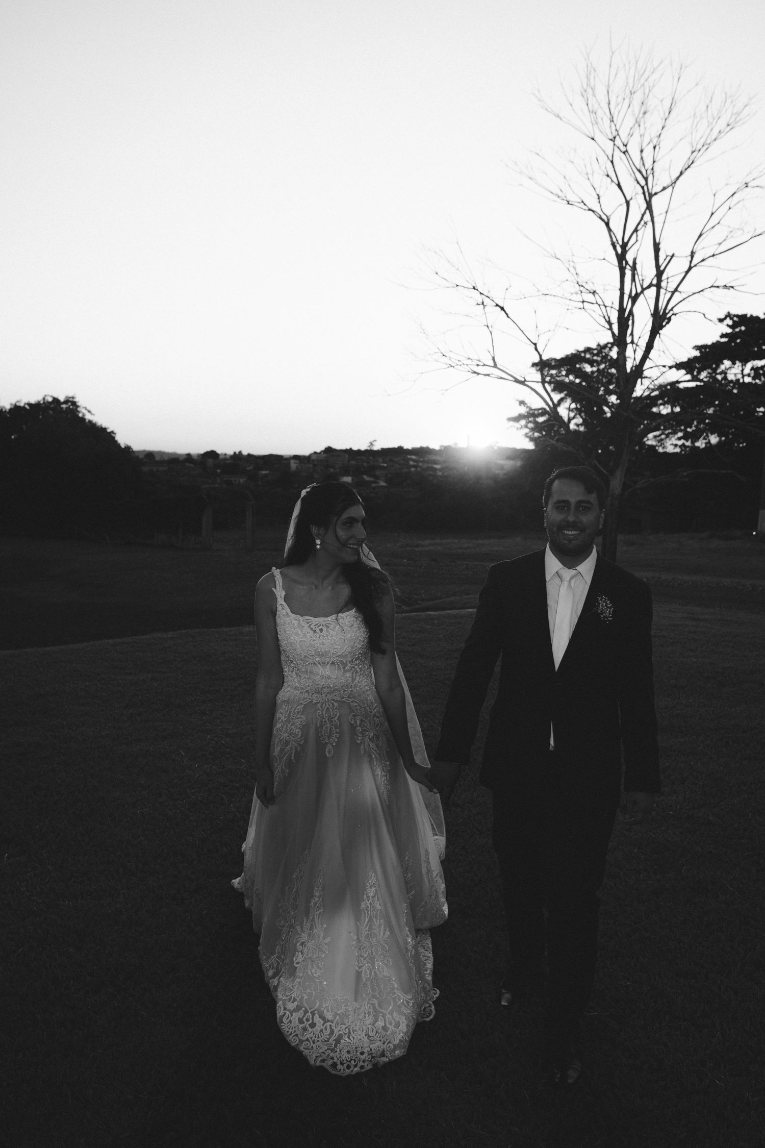 Black and white photo of a bride and groom holding hands at sunset in an outdoor garden setting.