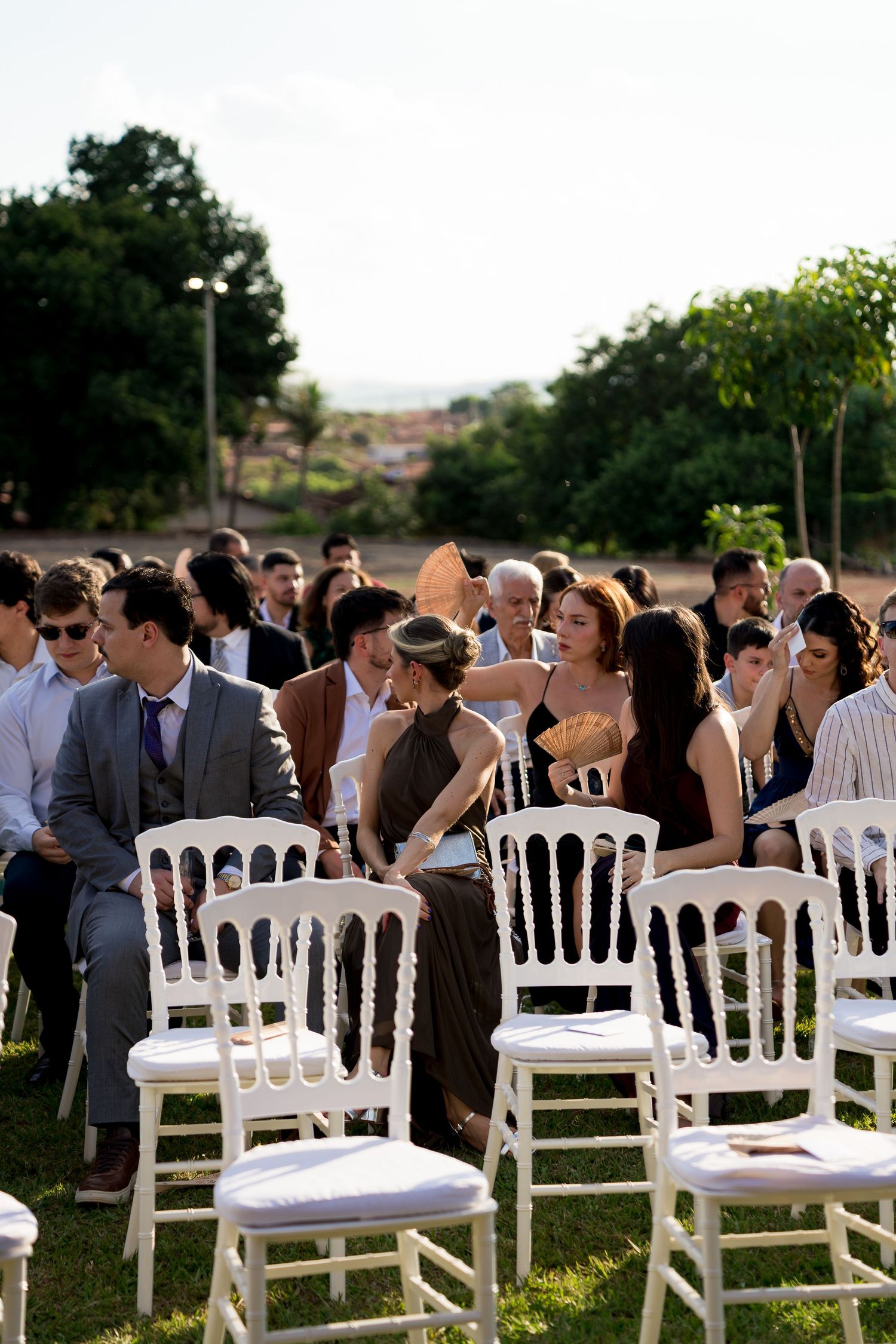 Guests seated on white chairs at an outdoor wedding ceremony on a sunny day.