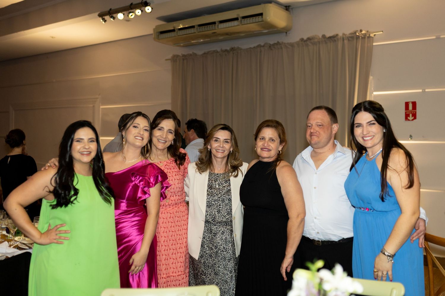 Group of seven adults posing together at an elegant indoor event, dressed in colorful formal attire.