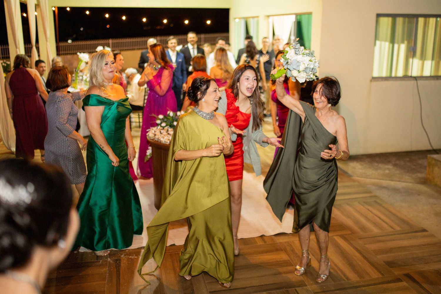 Women in elegant colorful gowns dancing and socializing at a formal wedding reception party.