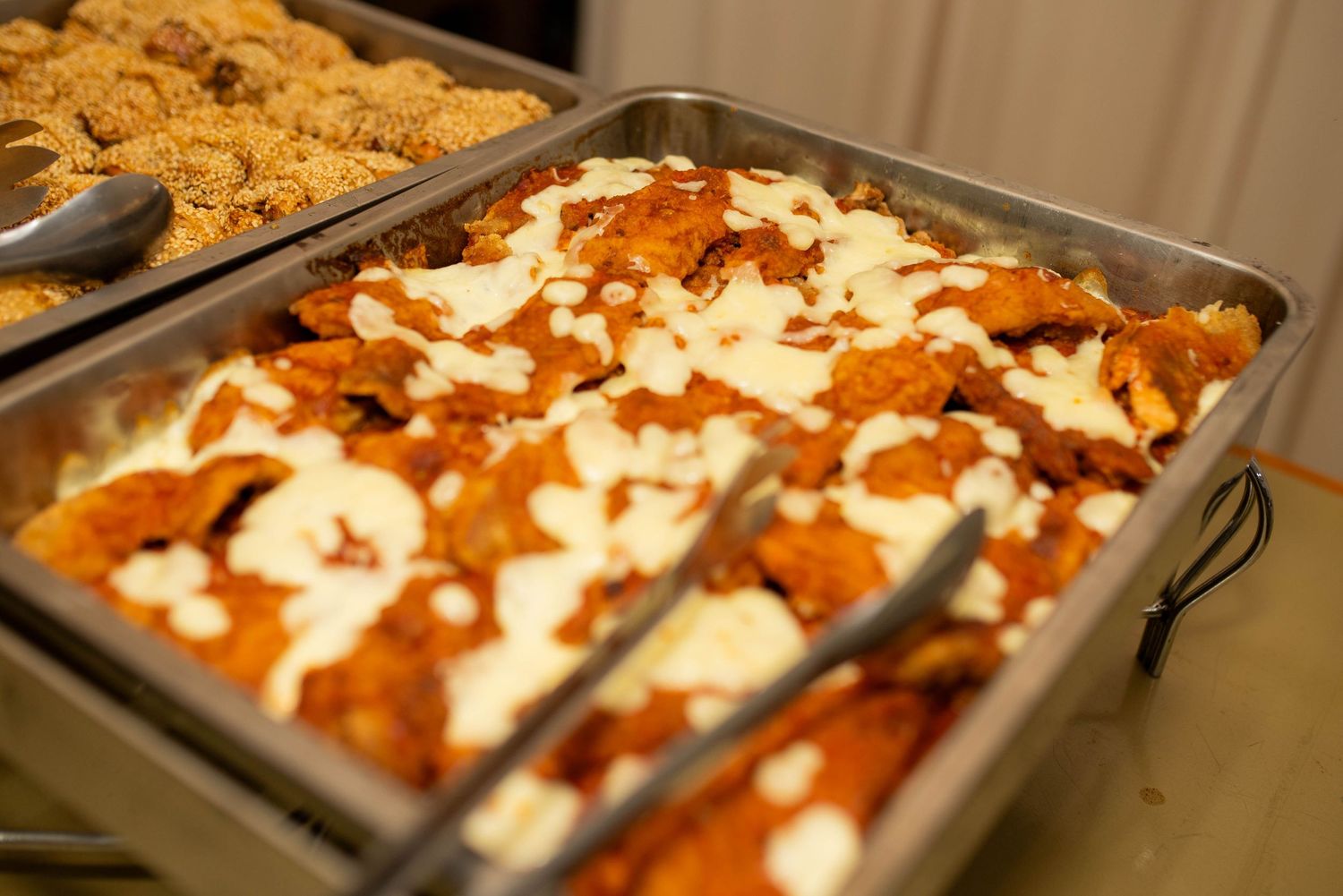 Buffet tray of enchiladas topped with orange sauce and white cream, served alongside a pan of crumbled topping.