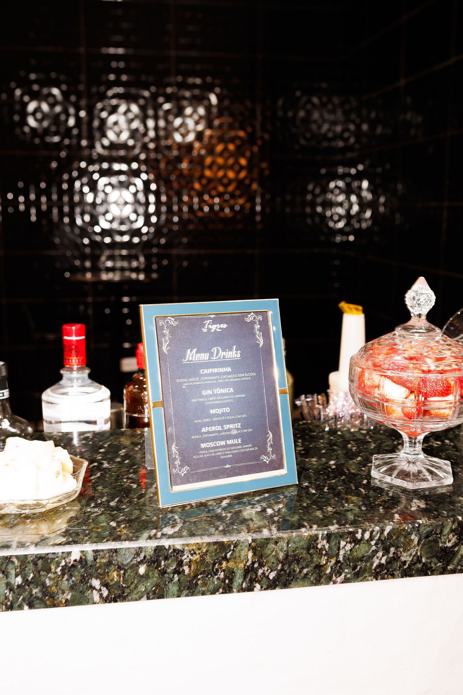 Elegant bar setup with a blue menu drinks sign on marble counter with crystal candy dish and liquor bottles.
