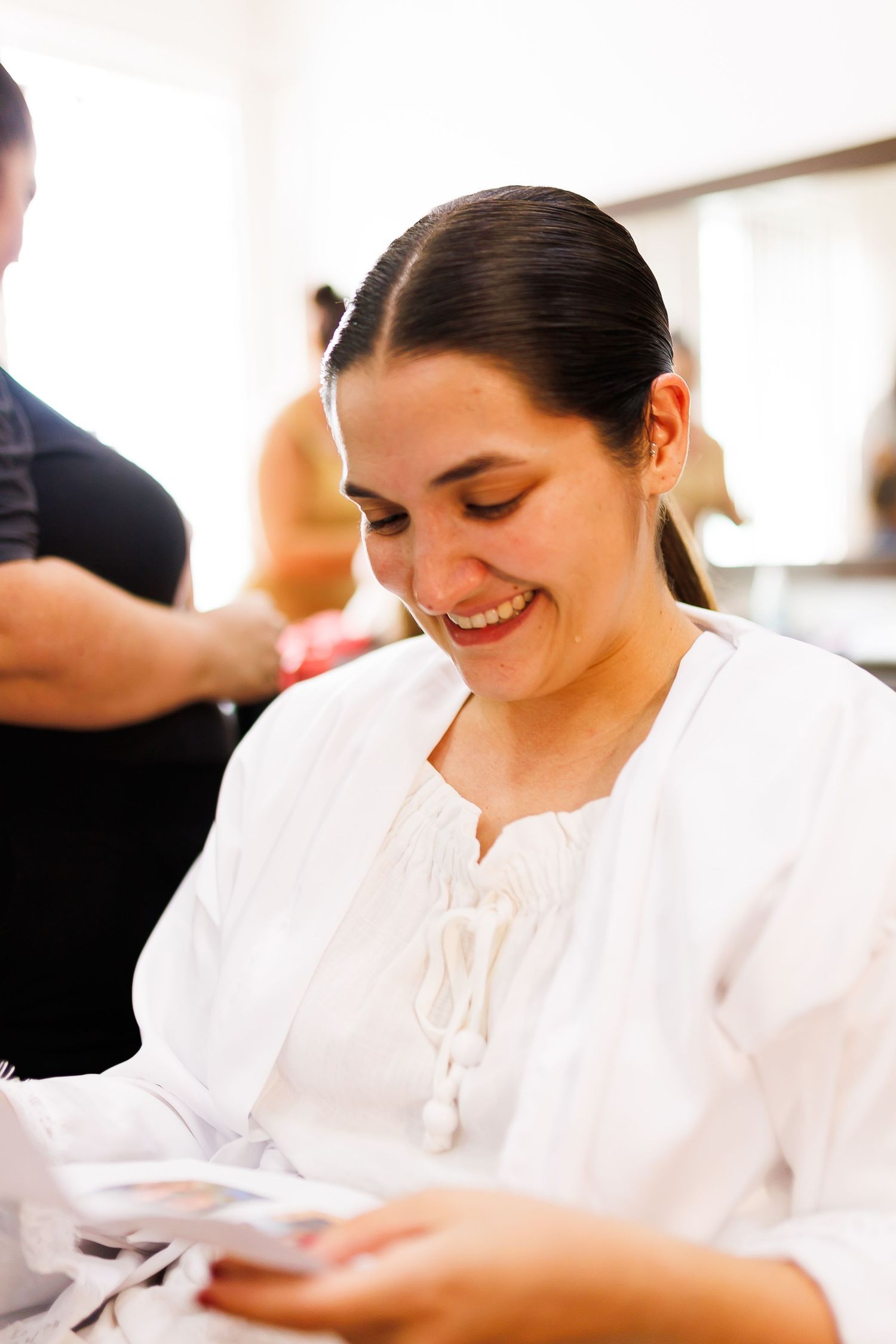 Smiling woman in white blouse looking down at cards in a bright salon setting.