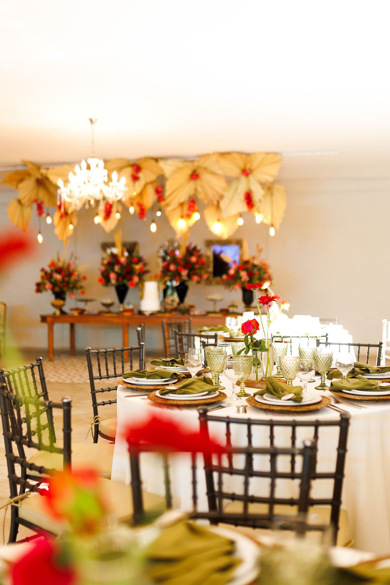 Elegant wedding reception venue with round tables, dark chairs, floral centerpieces, and gold leaf ceiling decor.
