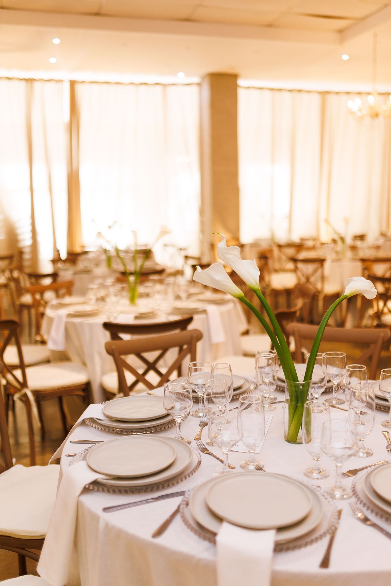 Elegant banquet hall with round tables set with white linens, crystal glasses, and calla lily centerpieces.