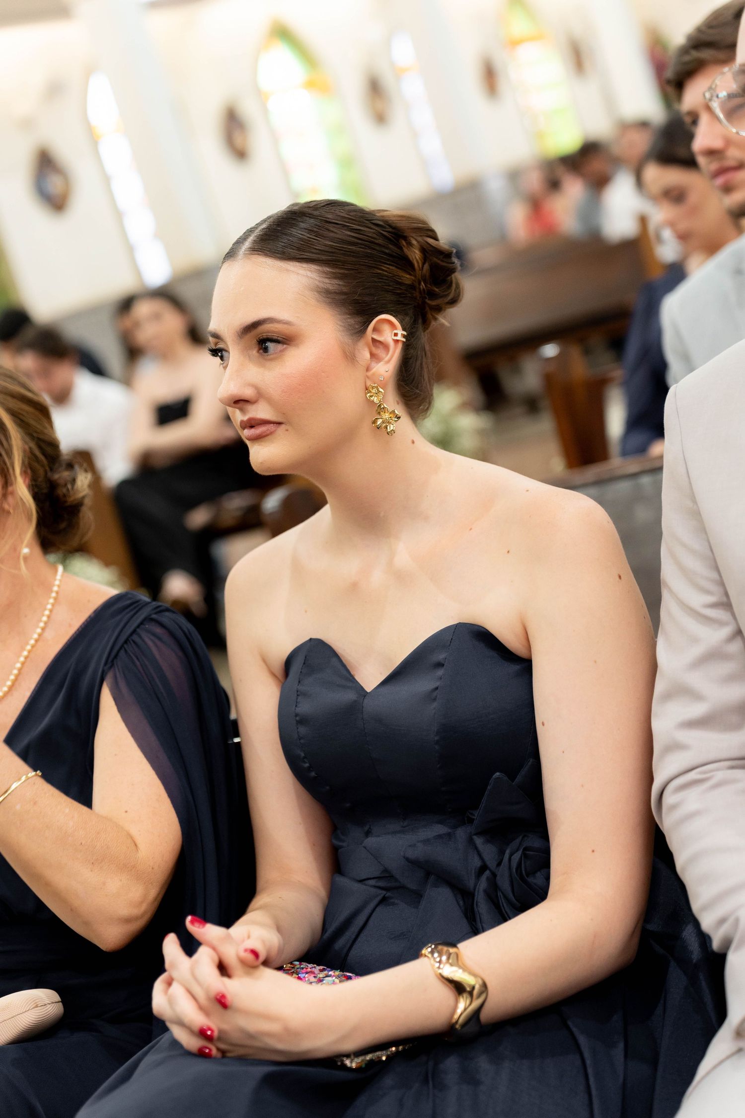 Elegant woman in navy strapless gown with gold earrings seated at a formal church event.