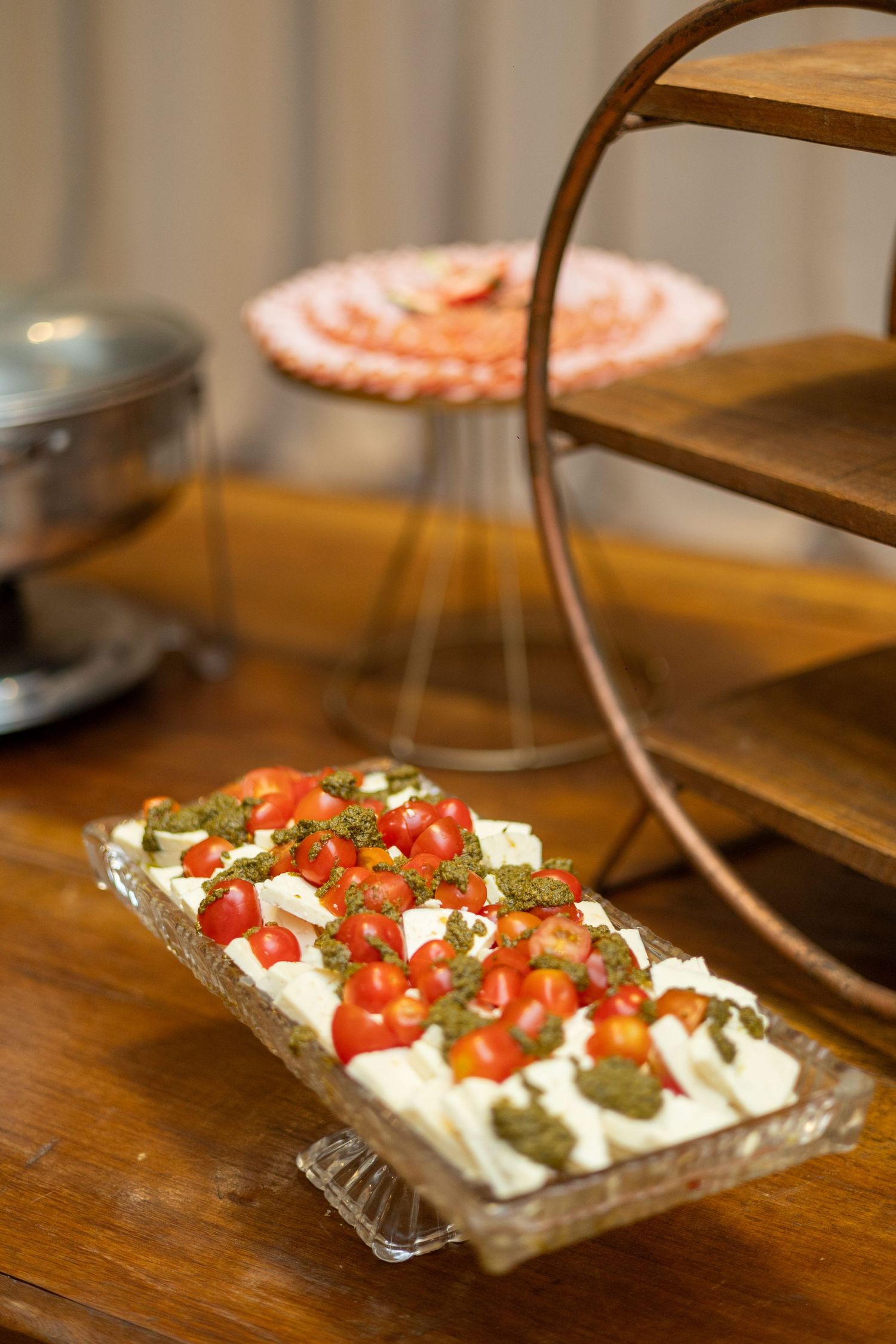 A rectangular tray of cream cheese topped with cherry tomatoes and pesto on a wooden table.