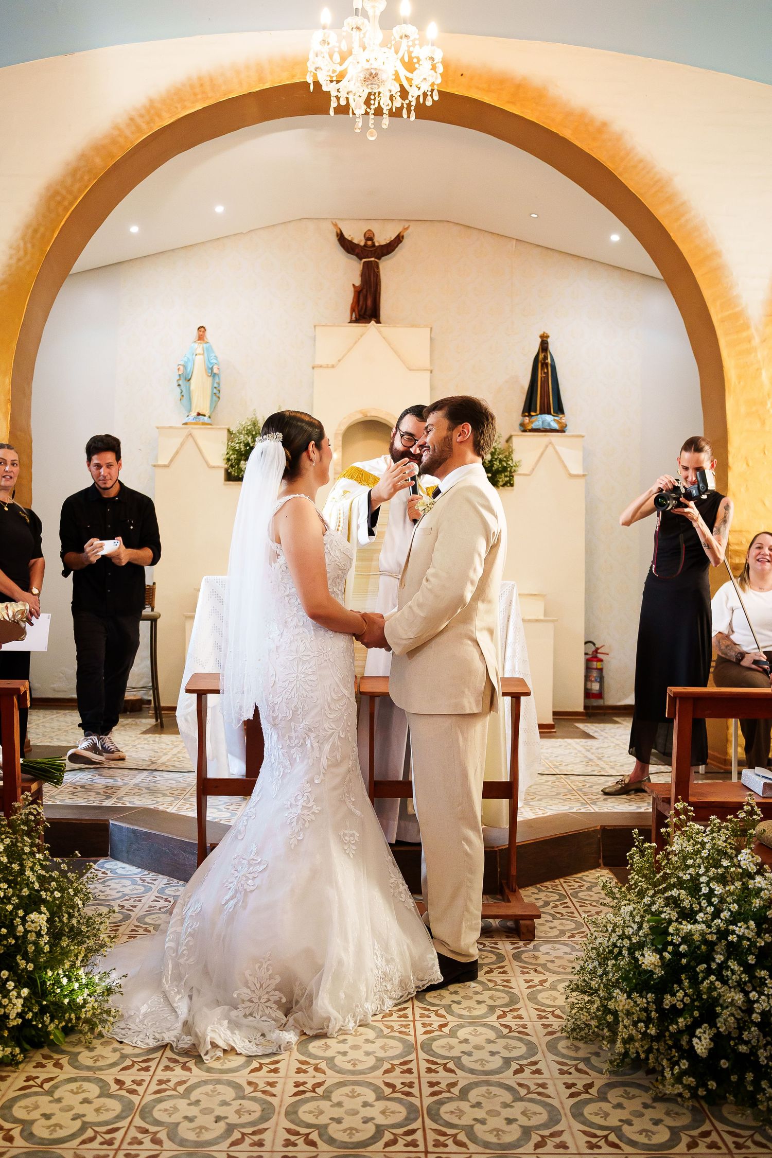 Bride and groom exchange vows at a charming chapel altar adorned with floral arrangements during their wedding ceremony.