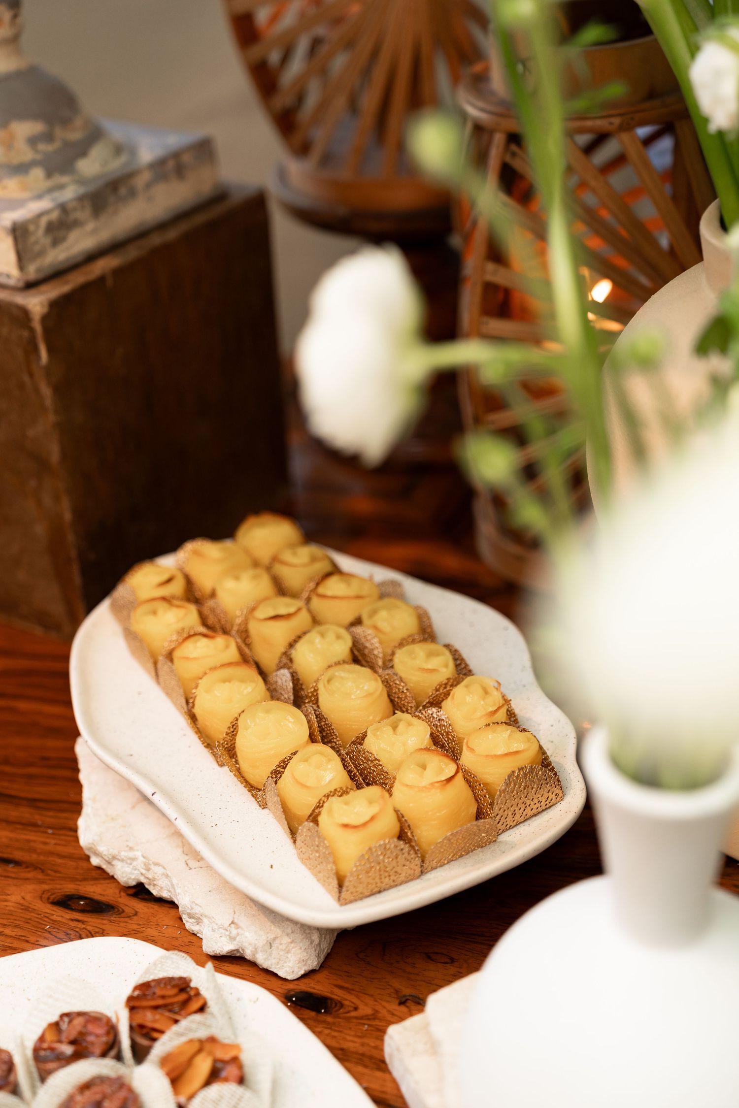 Elegant dessert table with golden mini pastries on a white platter, floral decor, and chocolate treats at a catered event.