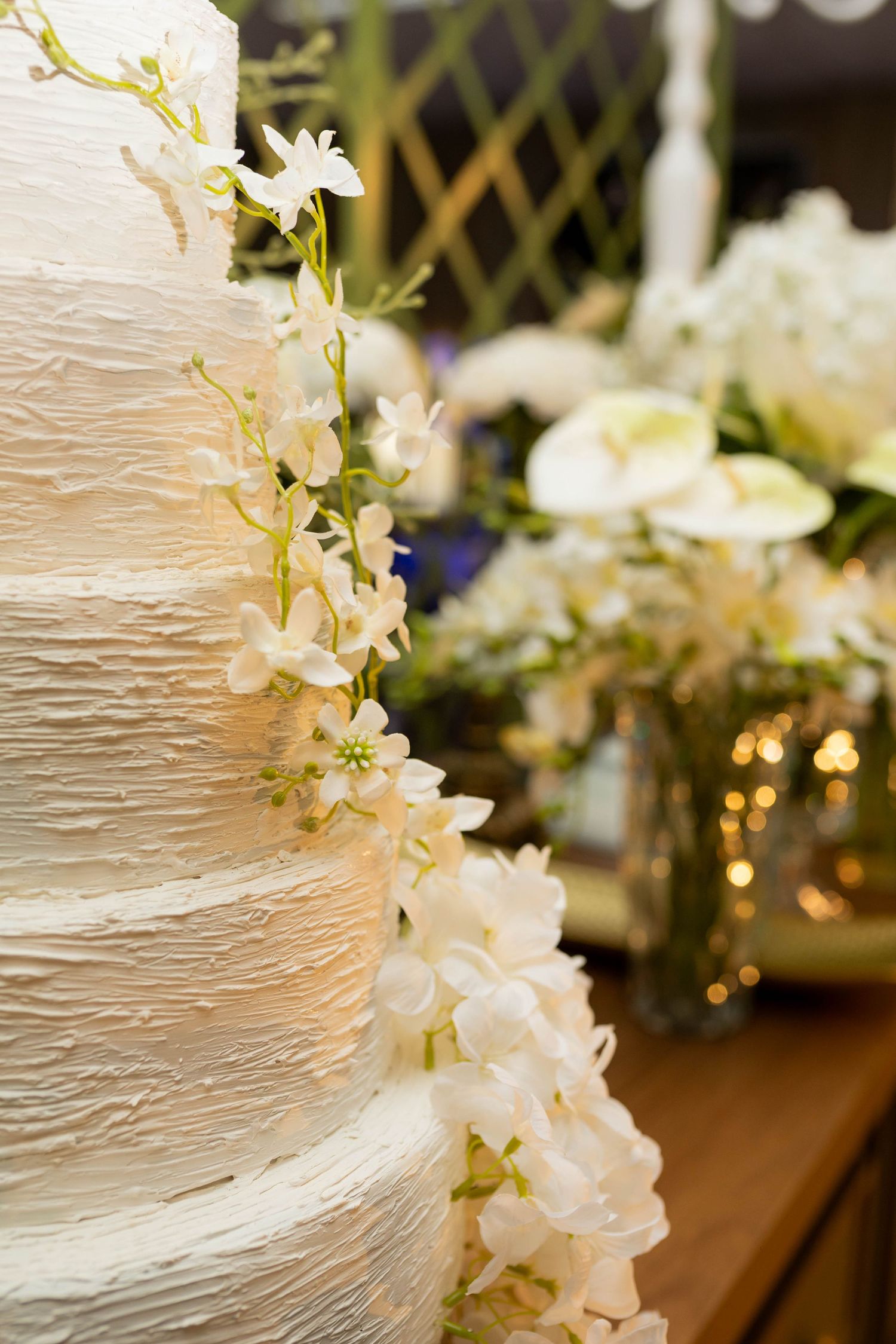 Elegant multi-tiered white wedding cake adorned with cascading white orchids and textured frosting on display.