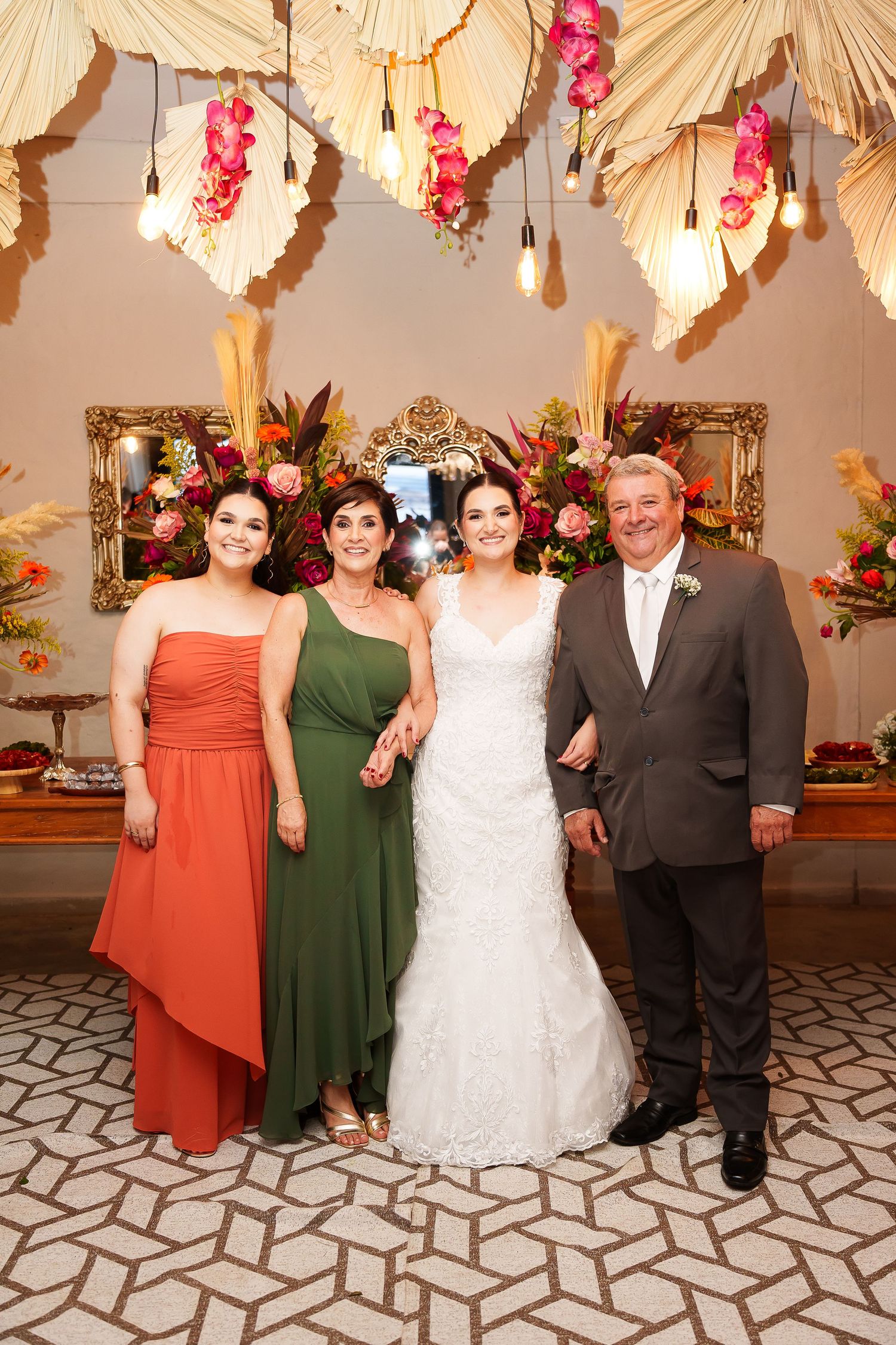 Bride in white gown poses with family at elegant wedding reception with tropical floral decor.
