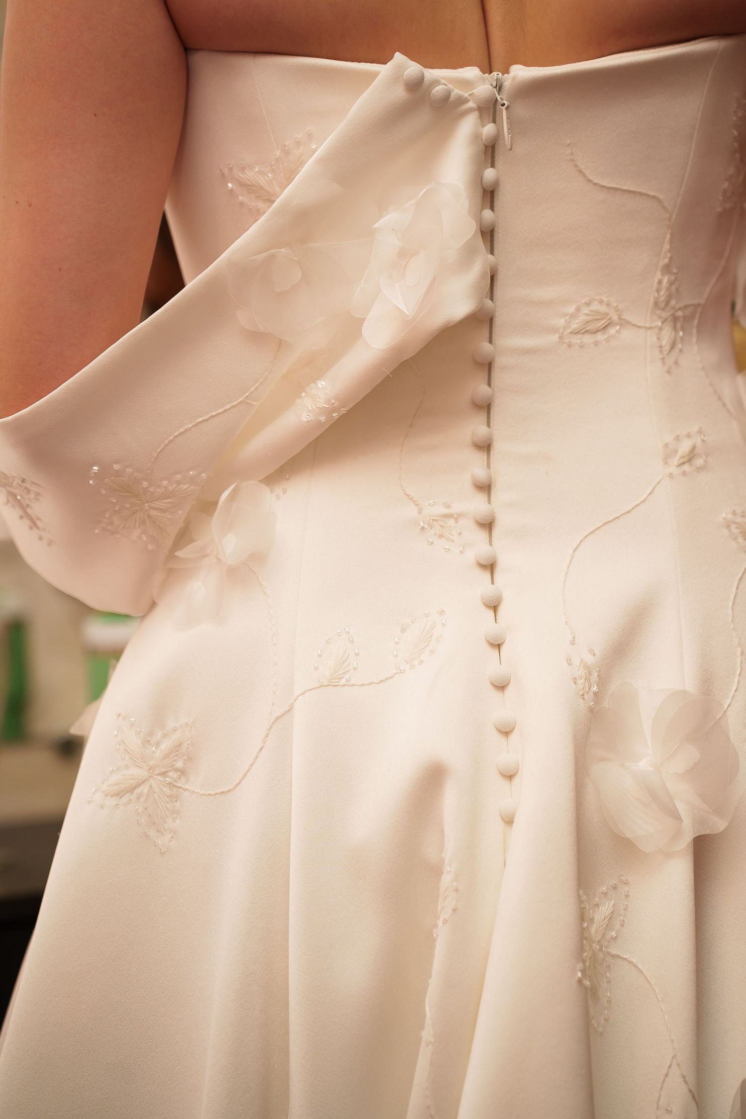 Close-up of a white wedding dress back with delicate buttons, floral embroidery, and elegant satin fabric detailing.