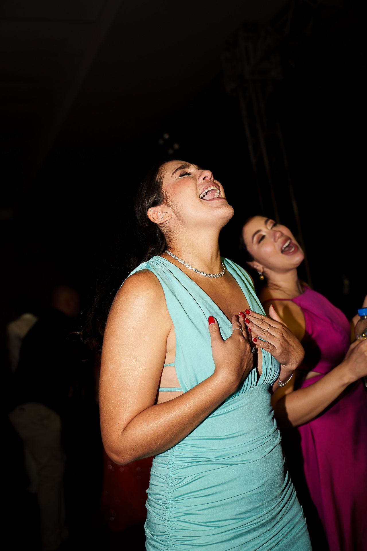 Two women in elegant dresses laugh and dance joyfully at a formal evening event.