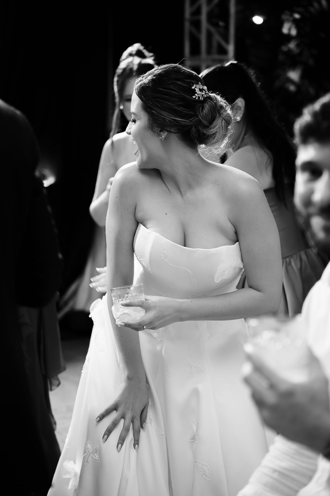 Black and white photo of a bride in a strapless white gown at a wedding reception, dancing with guests.
