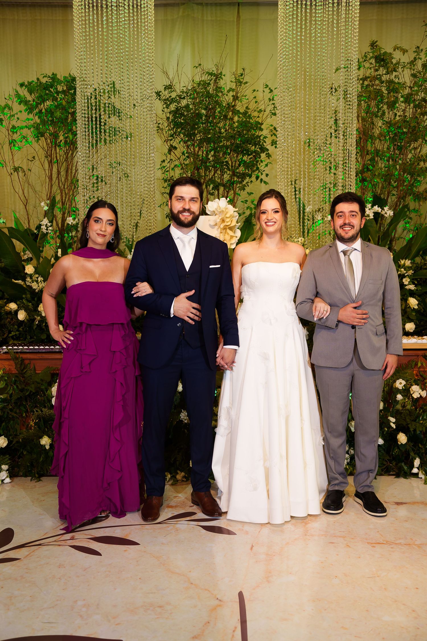Wedding party of four posing elegantly, bride in white gown, groom in navy suit, guests in purple dress and gray suit.