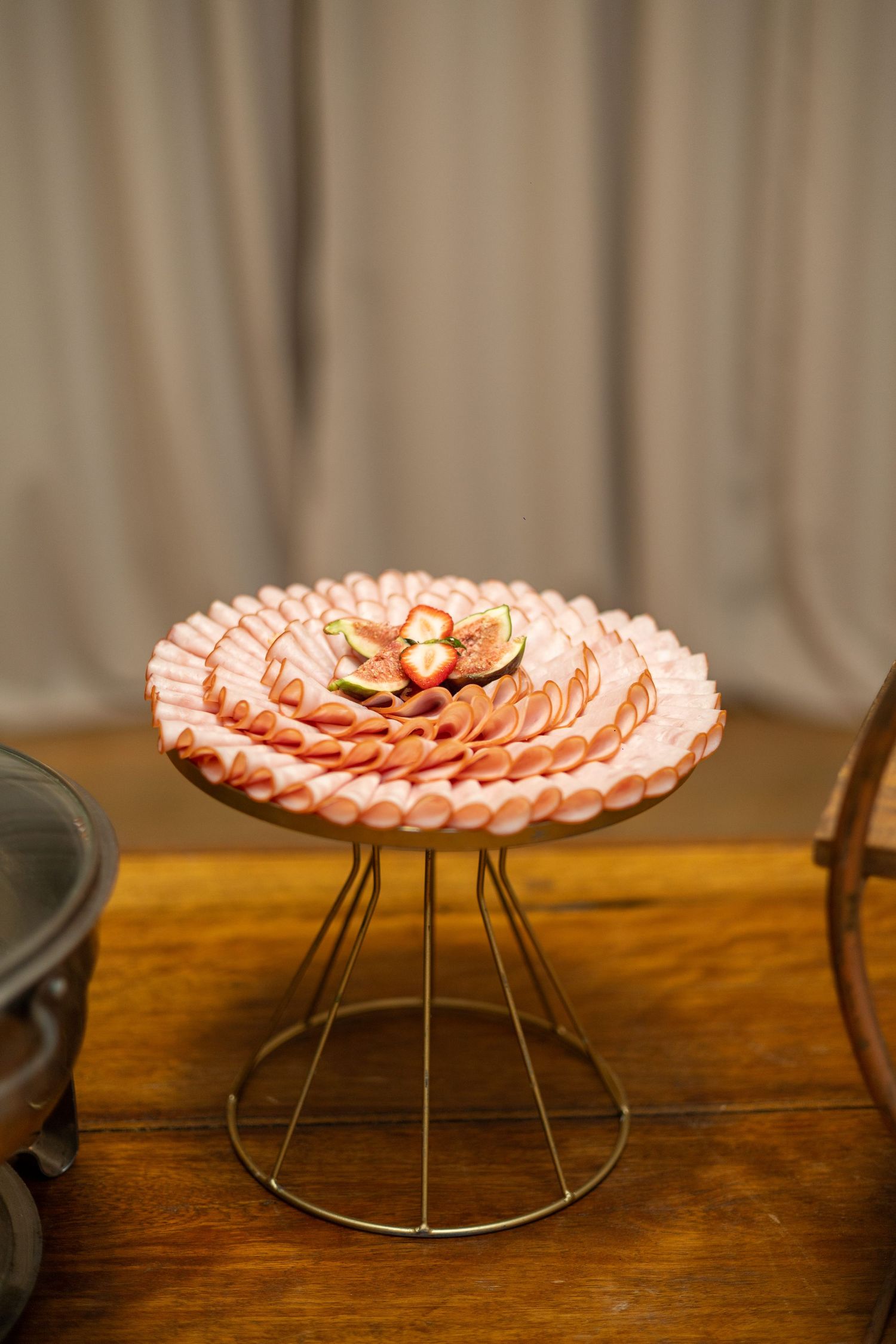 Elegant charcuterie display with sliced pink deli meat arranged in layers on a wire stand, topped with fresh figs.