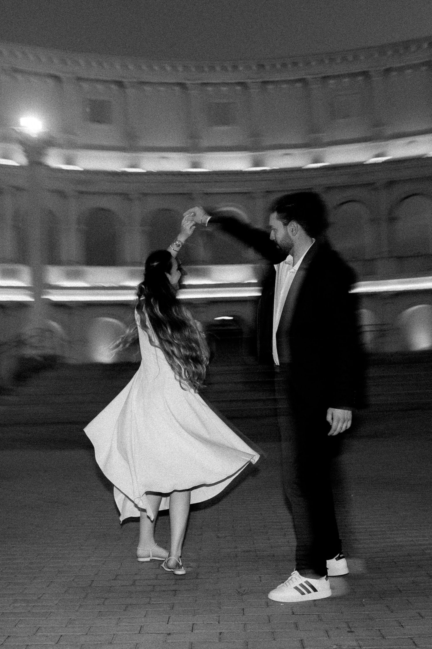 Black and white photo of a couple dancing at night in front of a historic Roman amphitheater.