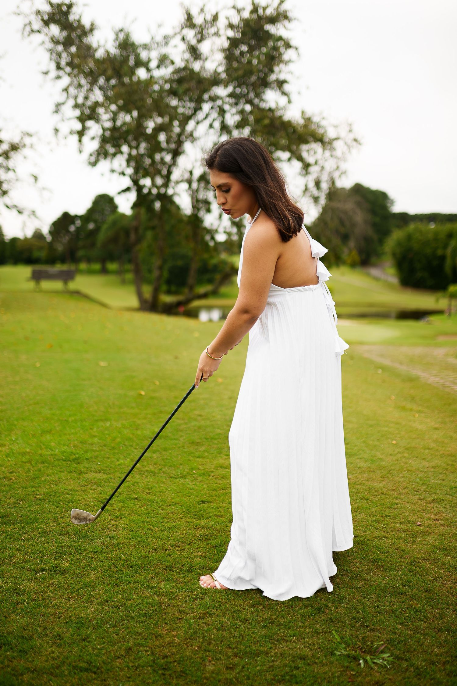 Woman in white backless dress playing golf on lush green course.