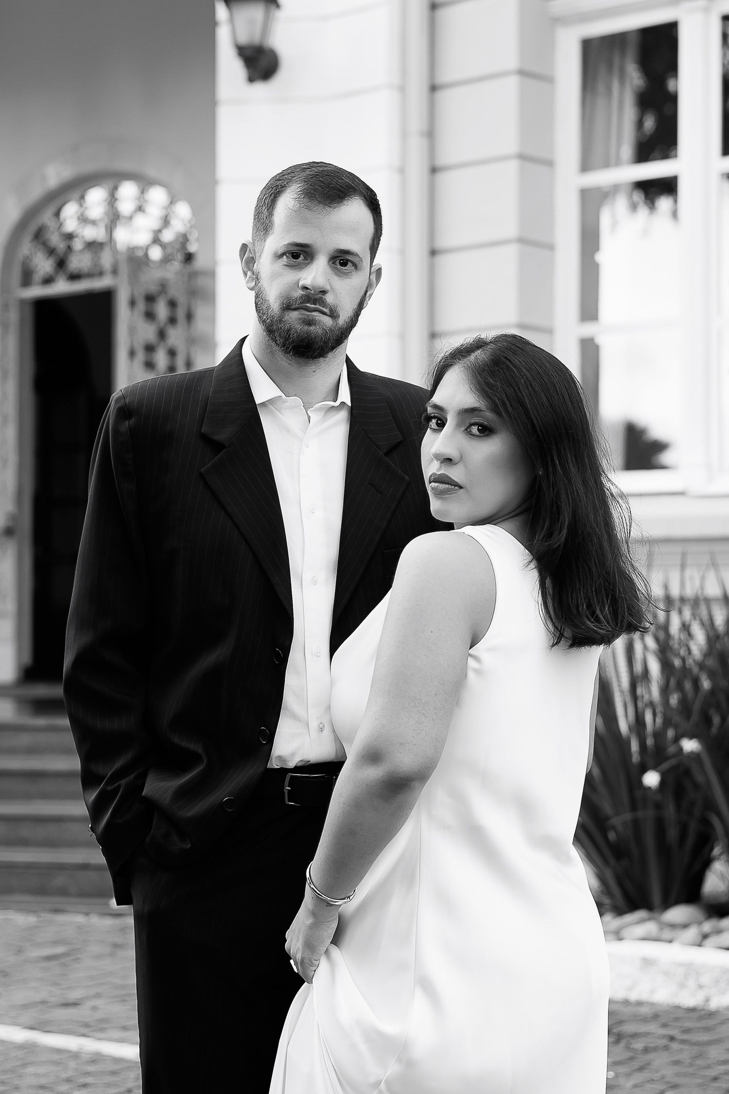 Black and white portrait of an elegant couple posing outdoors in front of a classic building.