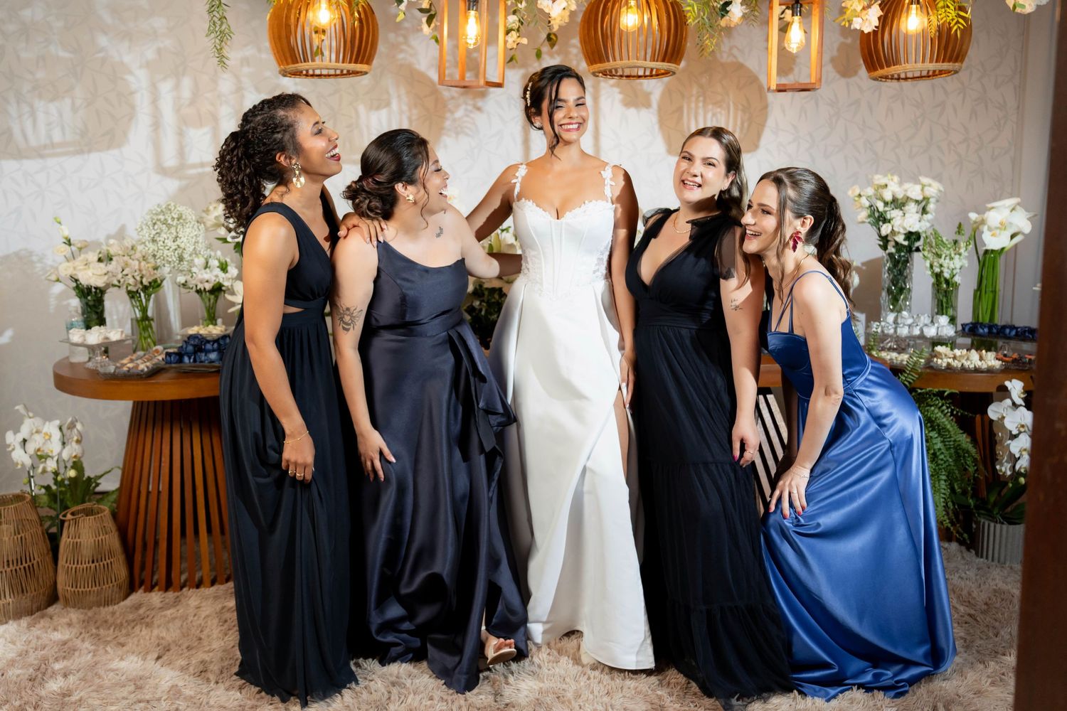 Bride in white gown poses with four bridesmaids in navy and blue dresses, smiling together in elegant floral decor.
