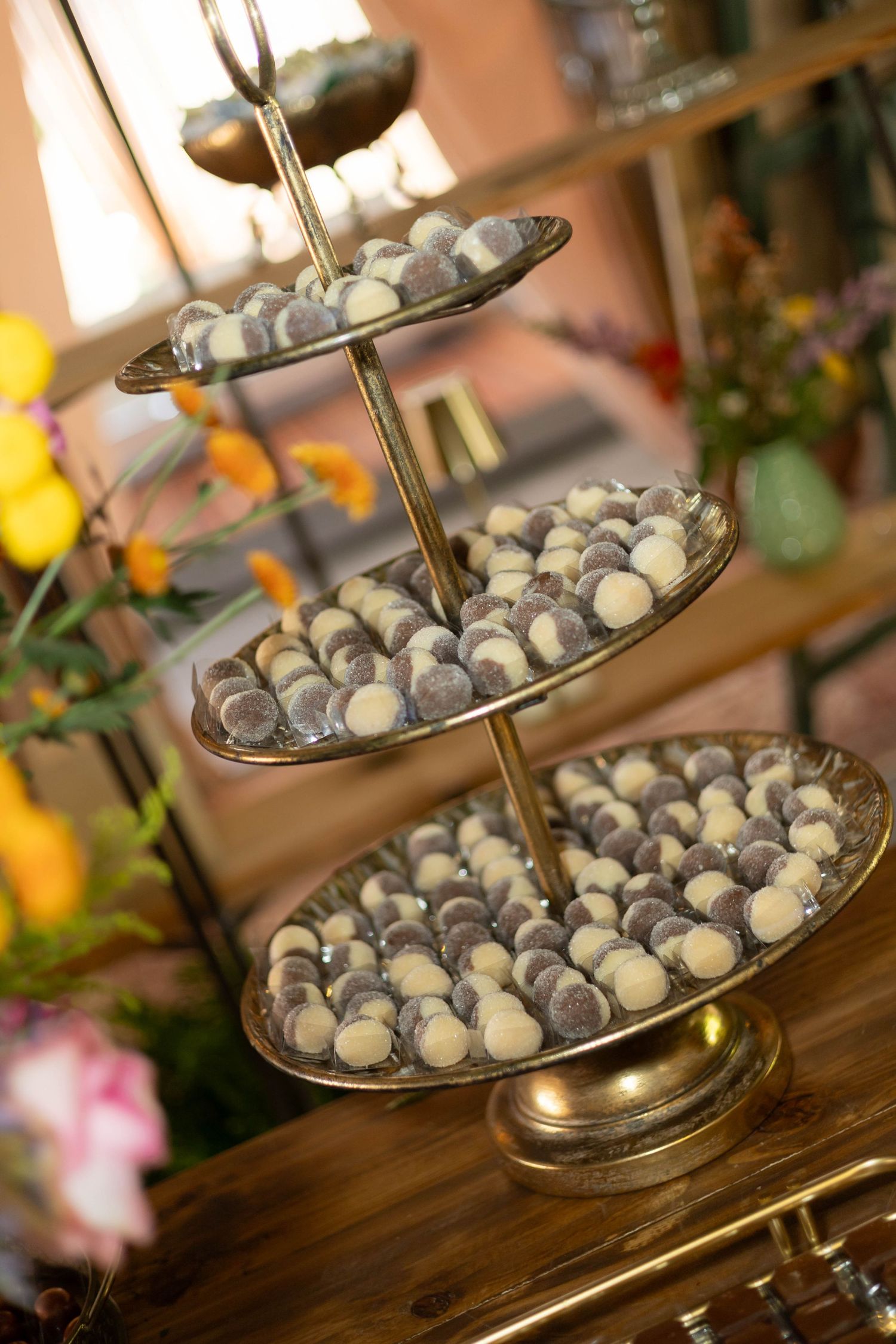 Three-tiered gold stand displaying chocolate and white truffles at an elegant wedding dessert table with floral decorations.