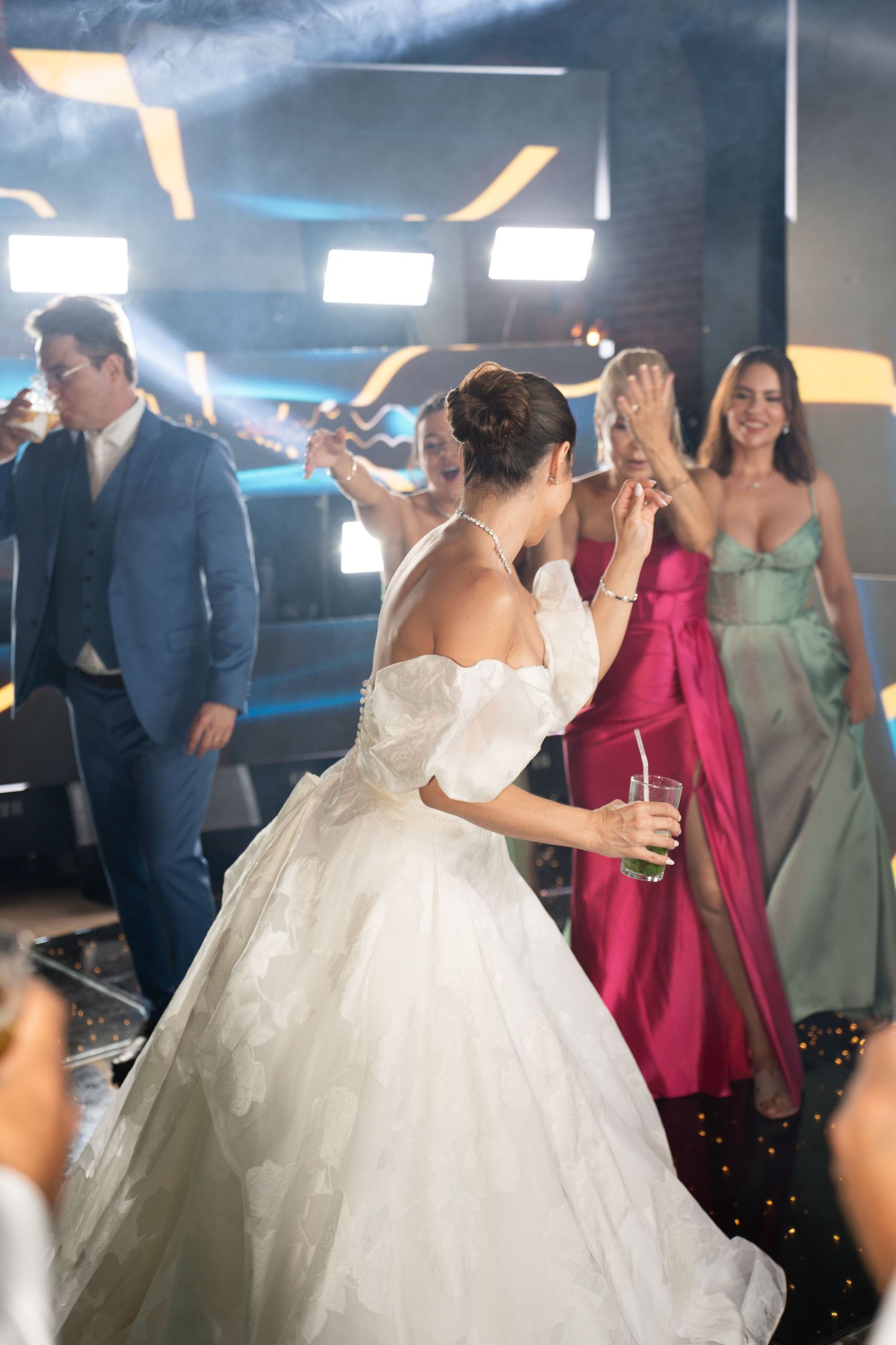 Bride in white ball gown dancing with guests in colorful formal attire at a wedding reception.