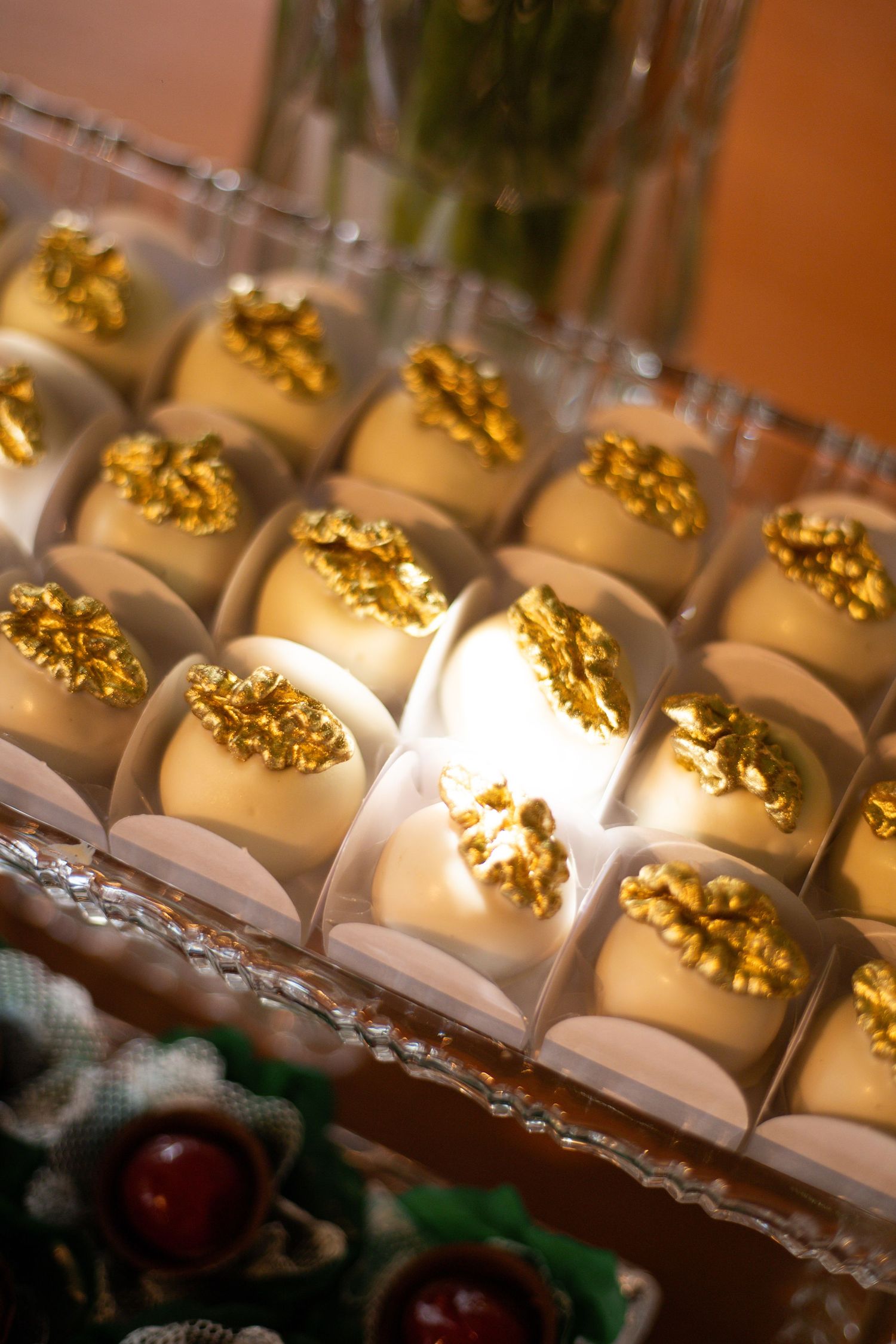 Elegant white chocolate truffles topped with gold leaf decorations displayed in clear individual cups on a crystal tray.