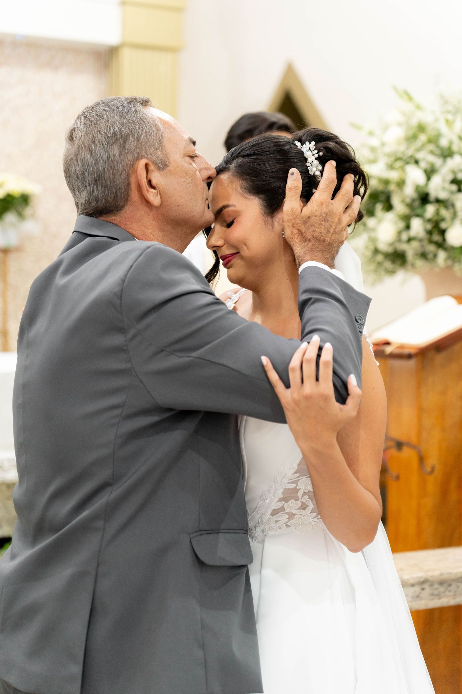 Father of the bride kissing his daughter on the forehead during an emotional wedding ceremony in a church.