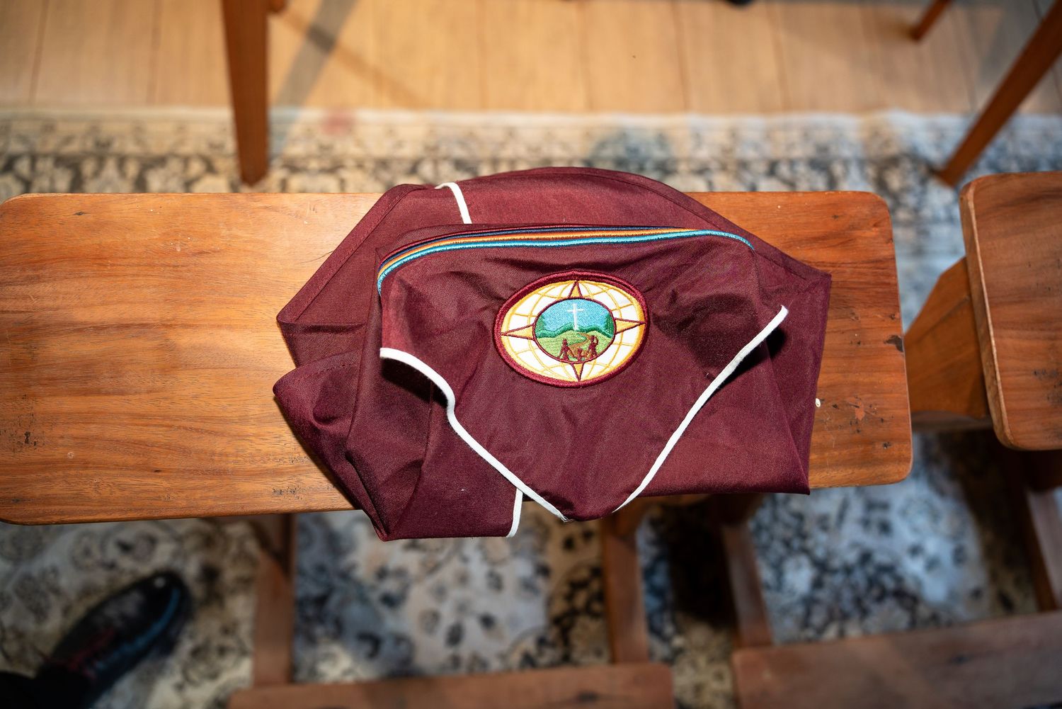 Maroon jacket with compass patch logo displayed on wooden bench at indoor event.