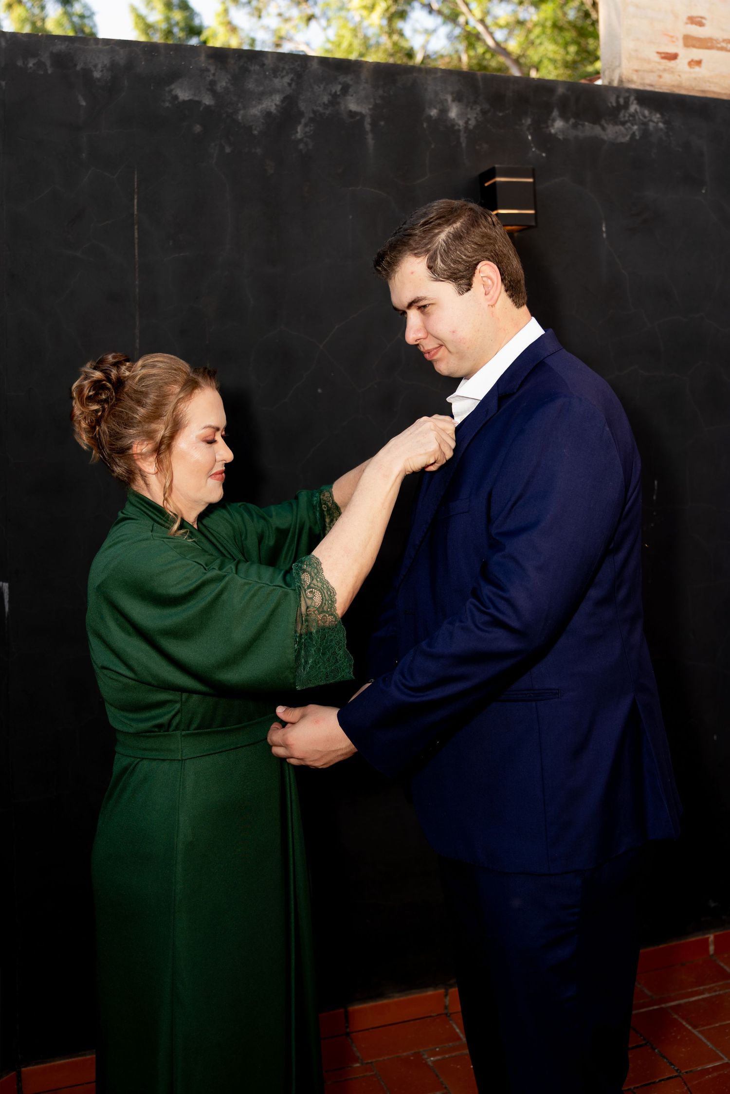 Woman in green dress pinning boutonniere on man in navy suit at formal event.