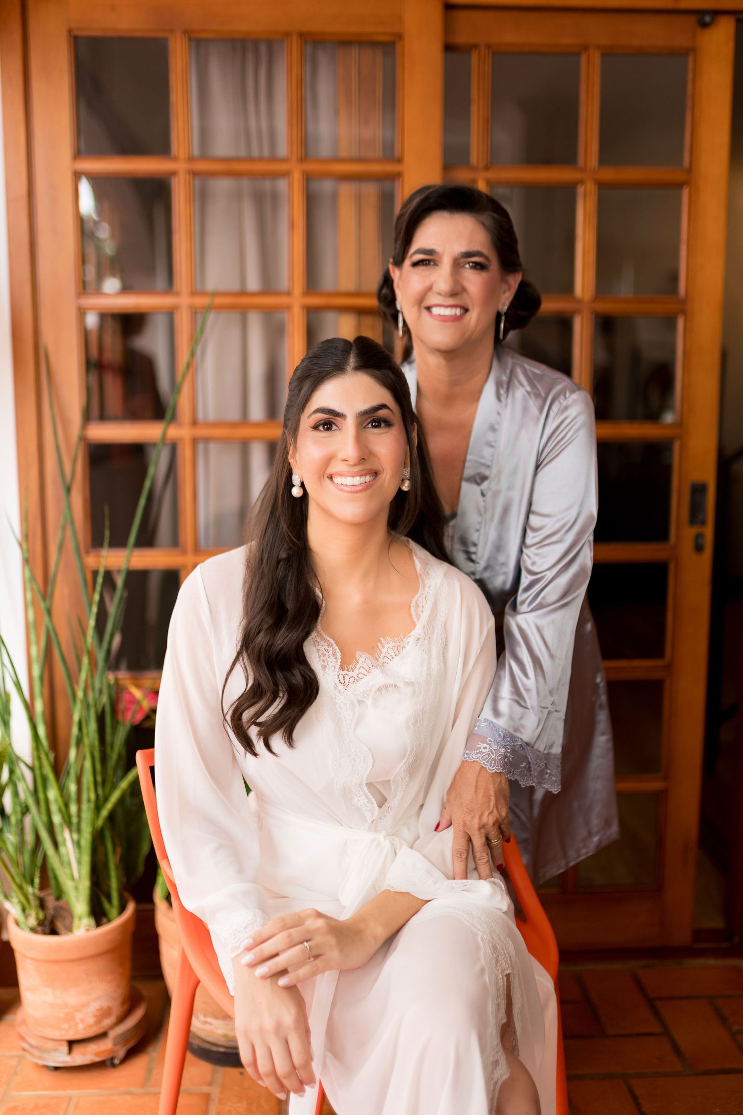 Bride and bridesmaid in robes smiling together during wedding preparations indoors.