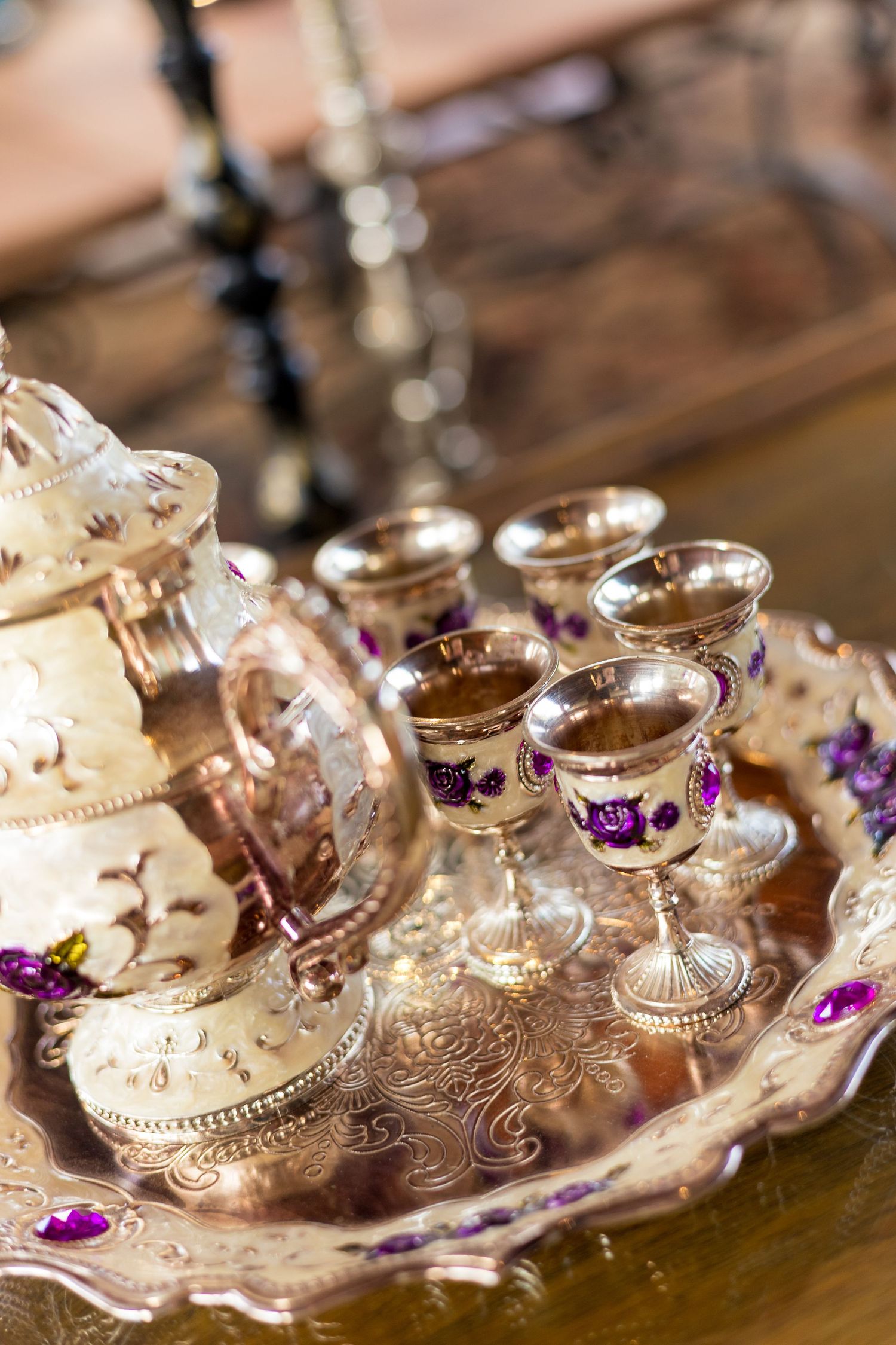 Ornate gold tea set with purple gemstone accents on decorative tray, featuring goblets and teapot with floral designs.