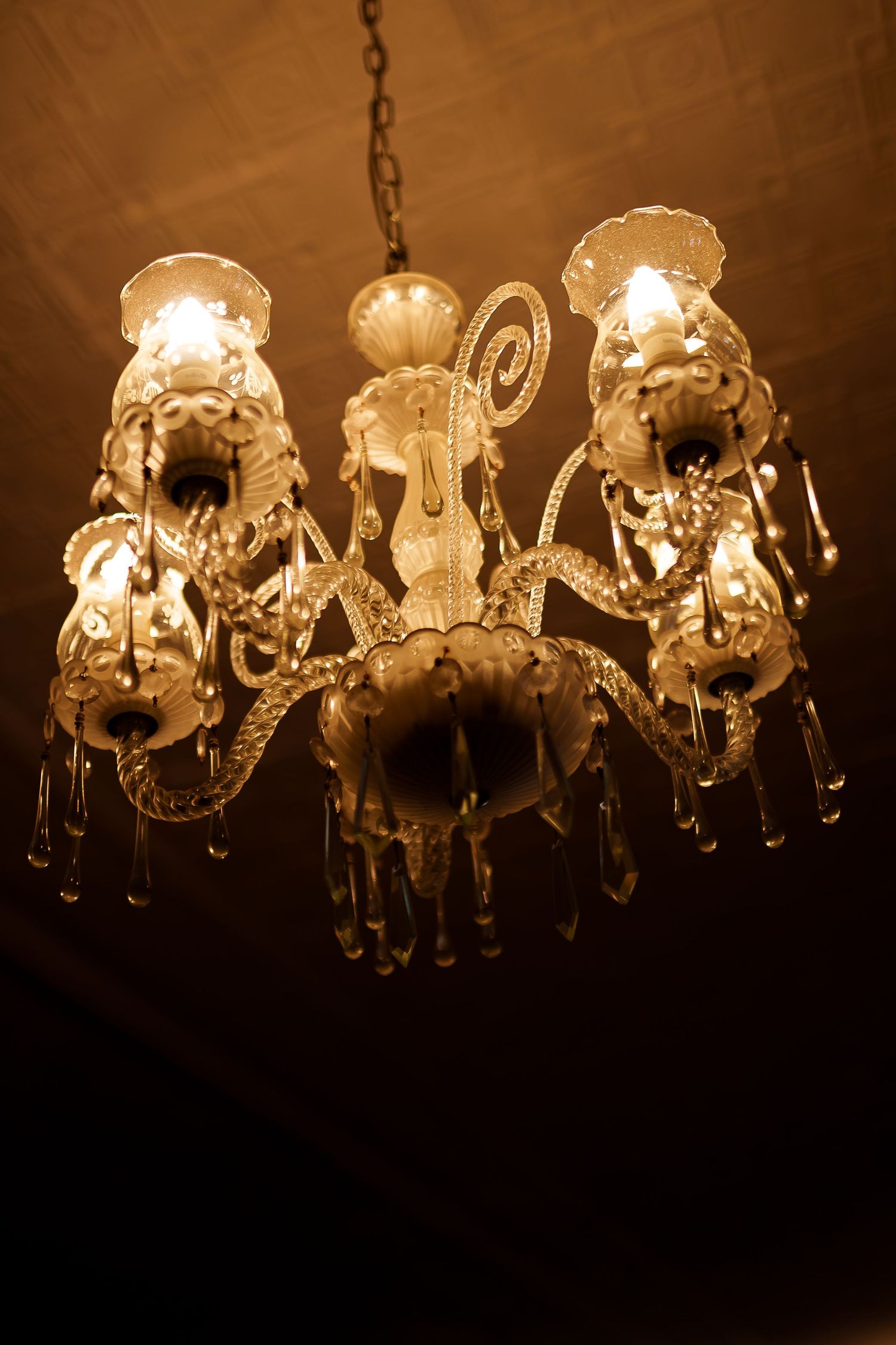 Elegant vintage crystal chandelier with warm glowing lights hanging from ceiling in dark room.