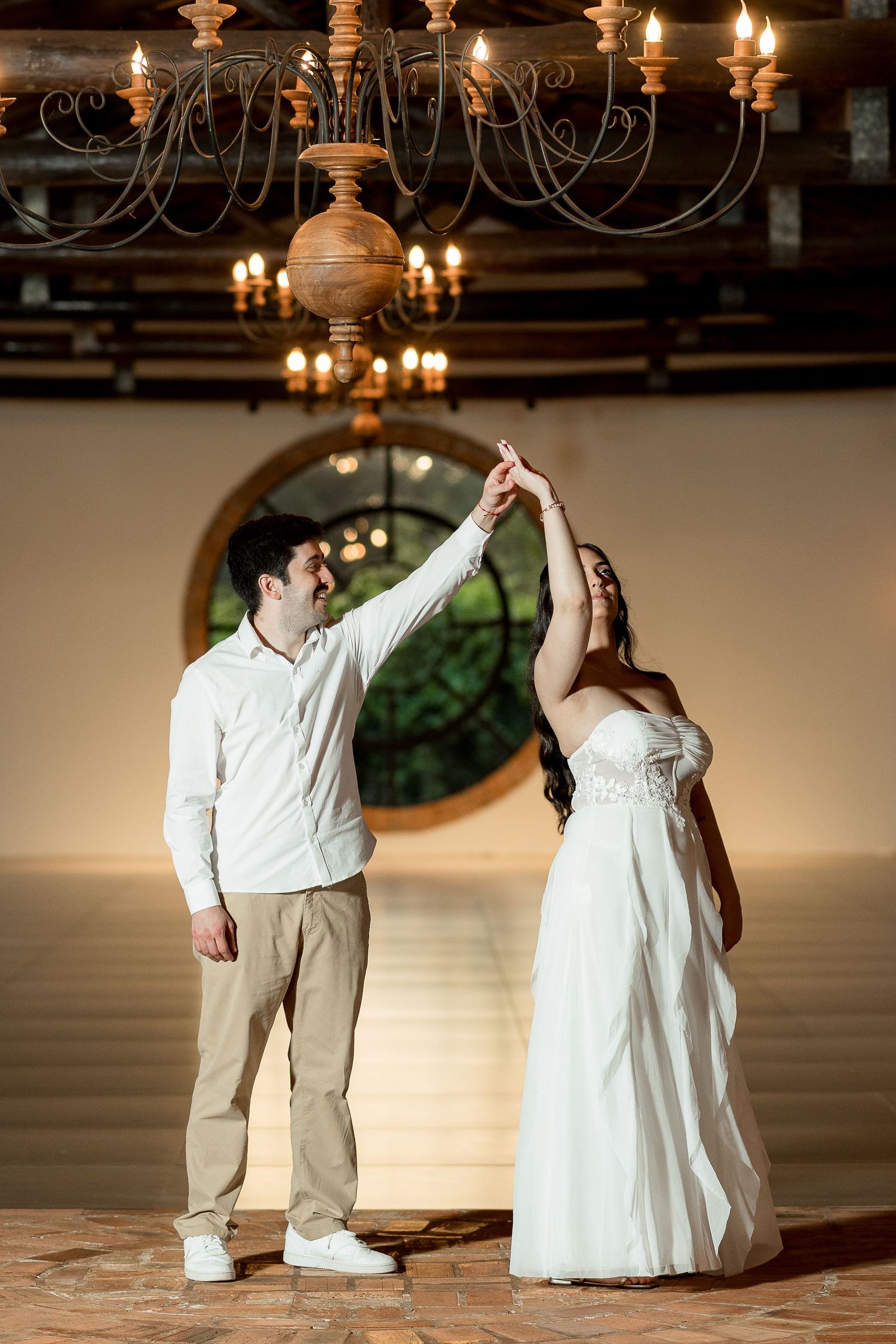 Bride and groom share a romantic dance under a chandelier in an elegant venue, with the groom spinning his bride in a white gown.