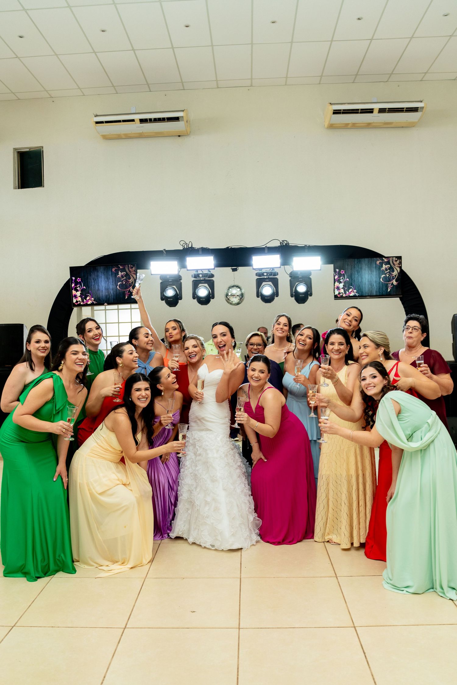 Bride in white gown poses with bridesmaids in colorful dresses at wedding reception venue.