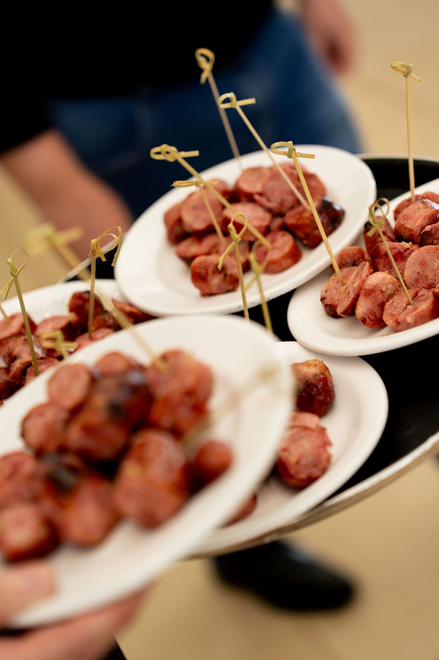 Catered appetizer plates of sliced sausages with decorative bamboo picks served on white plates at an event.