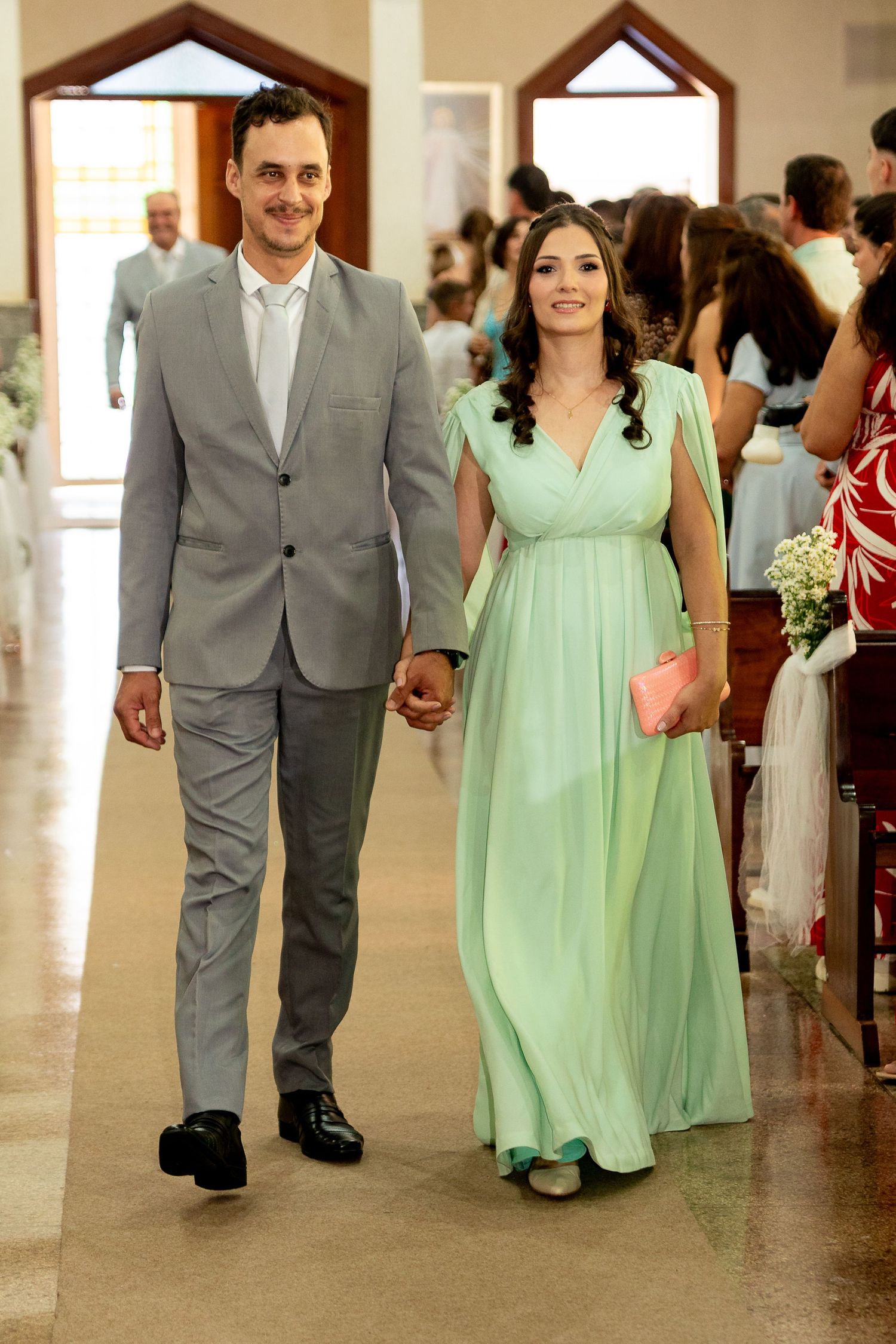 Couple walking down church aisle, man in gray suit, woman in mint green gown, holding hands at wedding.