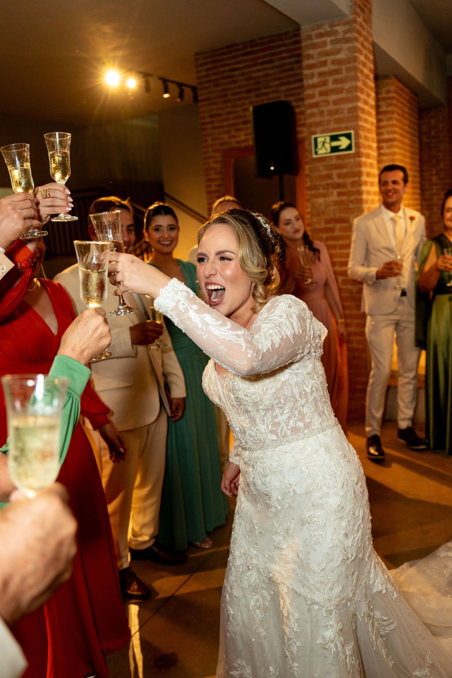 Bride in lace gown toasting champagne with guests at wedding reception, smiling joyfully.