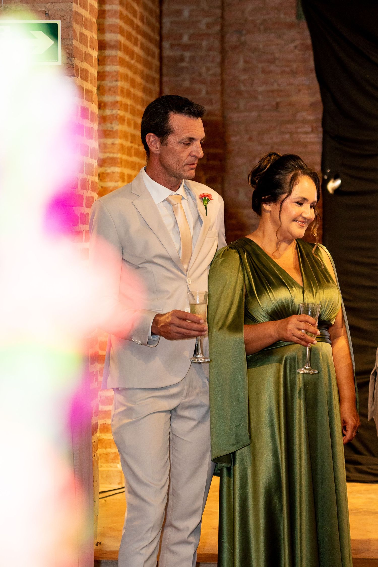Elegant couple in white suit and green gown holding champagne glasses at a wedding reception.