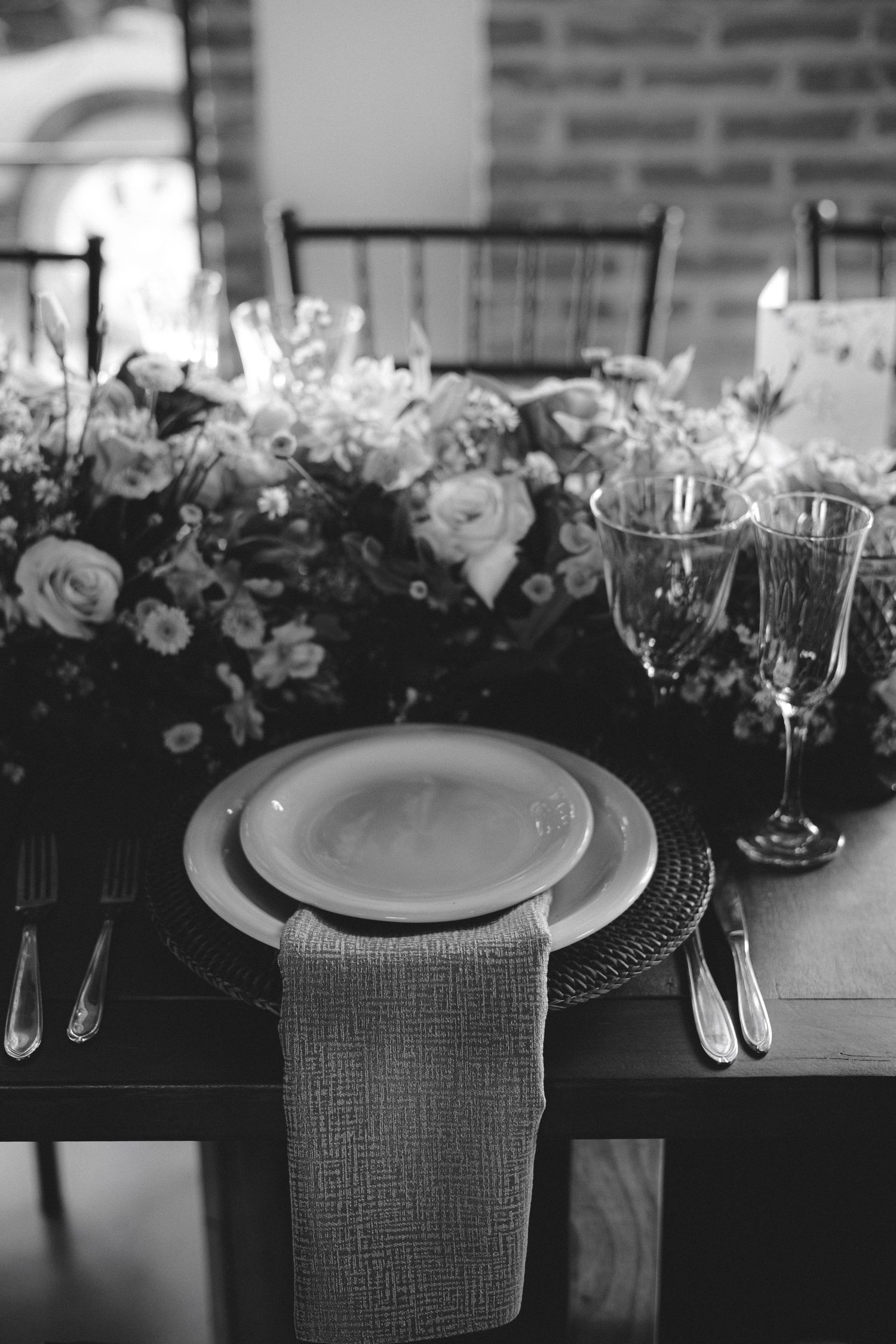 Elegant black and white wedding table setting with floral centerpiece, stacked plates, glassware, and linen napkin.