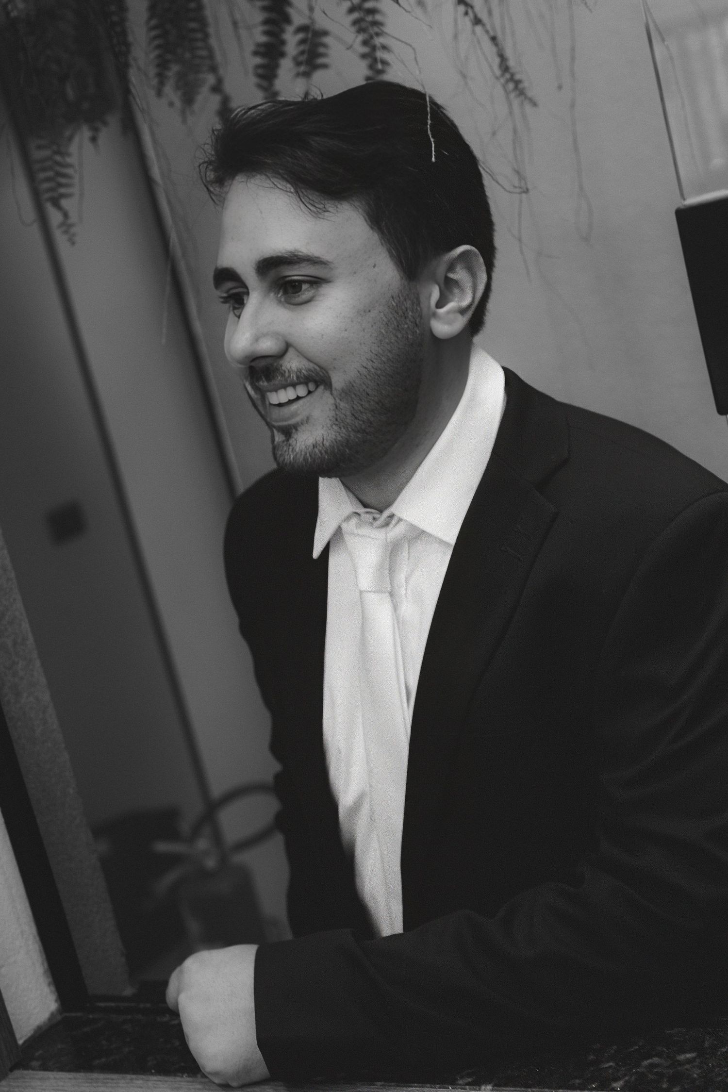 Black and white portrait of a smiling young man in a suit and tie, photographed outdoors.