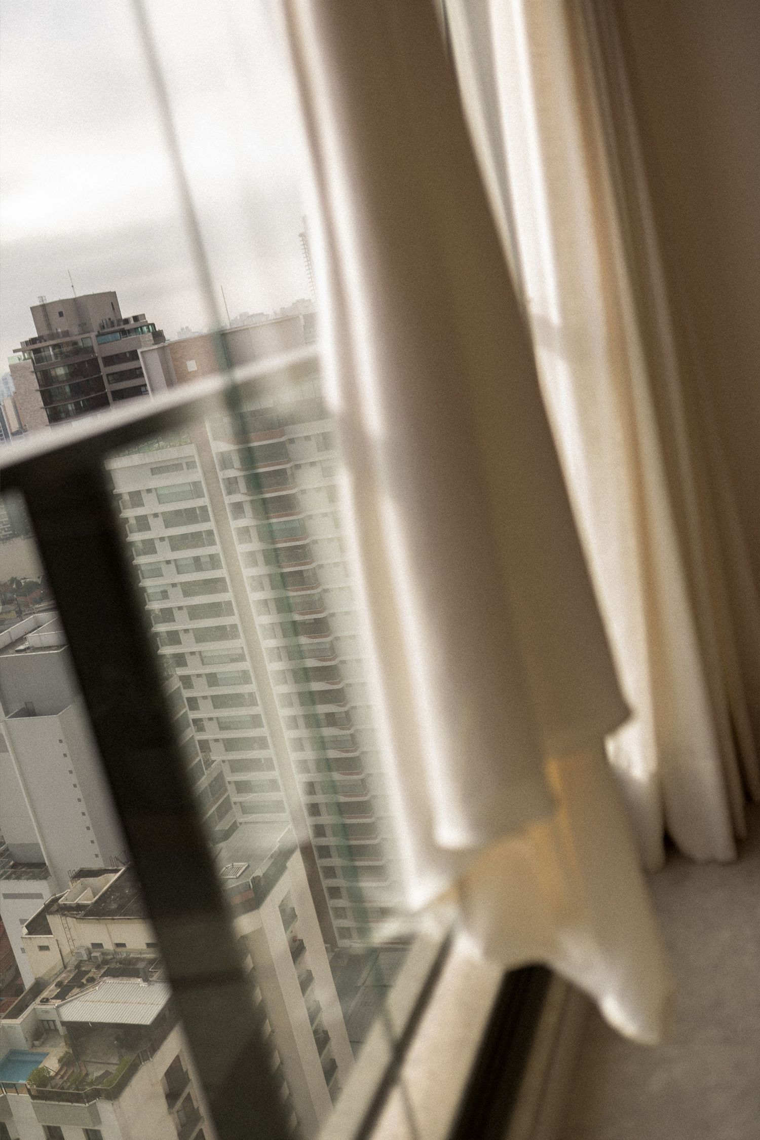 City skyline view through a window with elegant cream curtains in a high-rise building on an overcast day.