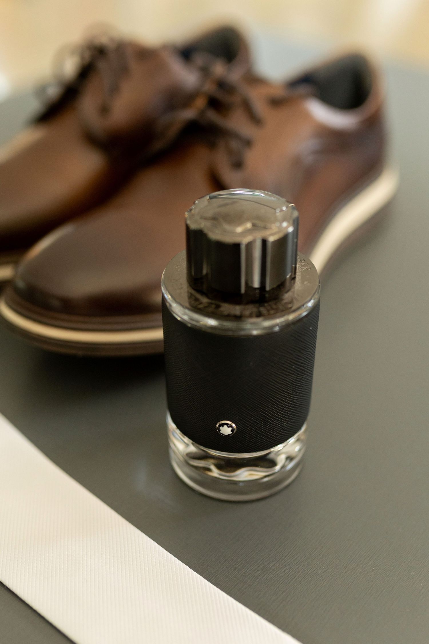 Montblanc cologne bottle displayed in front of brown leather dress shoes on a gray surface.