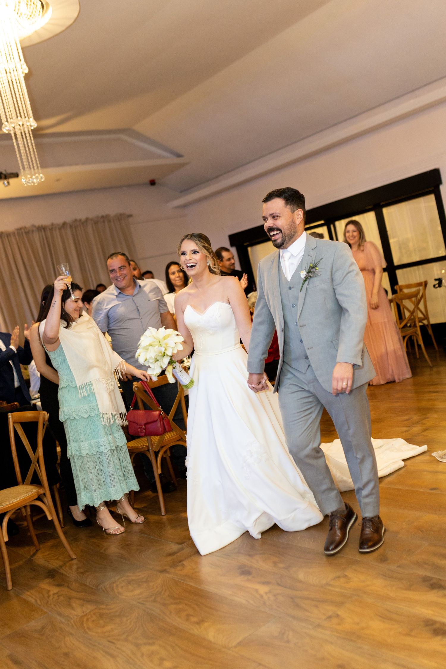 Bride in white gown and groom in gray suit walk joyfully down the aisle at their wedding reception.