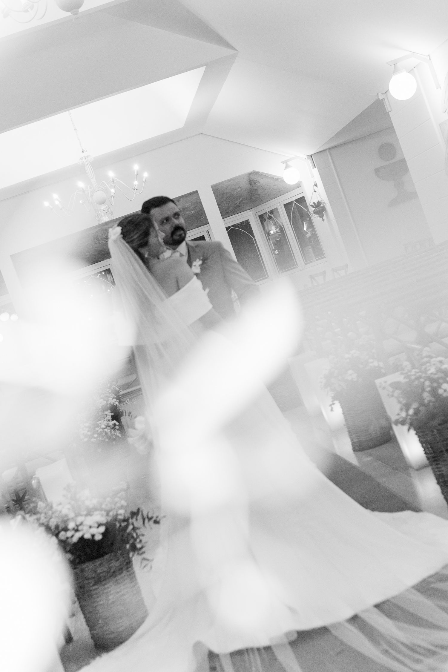 Black and white wedding photo of bride and groom sharing a tender moment, with soft bokeh foreground blur.