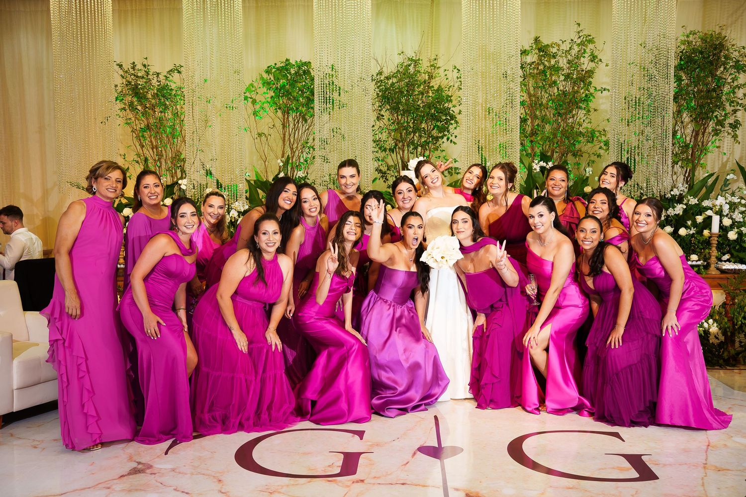 Bride in white gown surrounded by bridesmaids in matching fuchsia dresses posing together at elegant wedding reception.