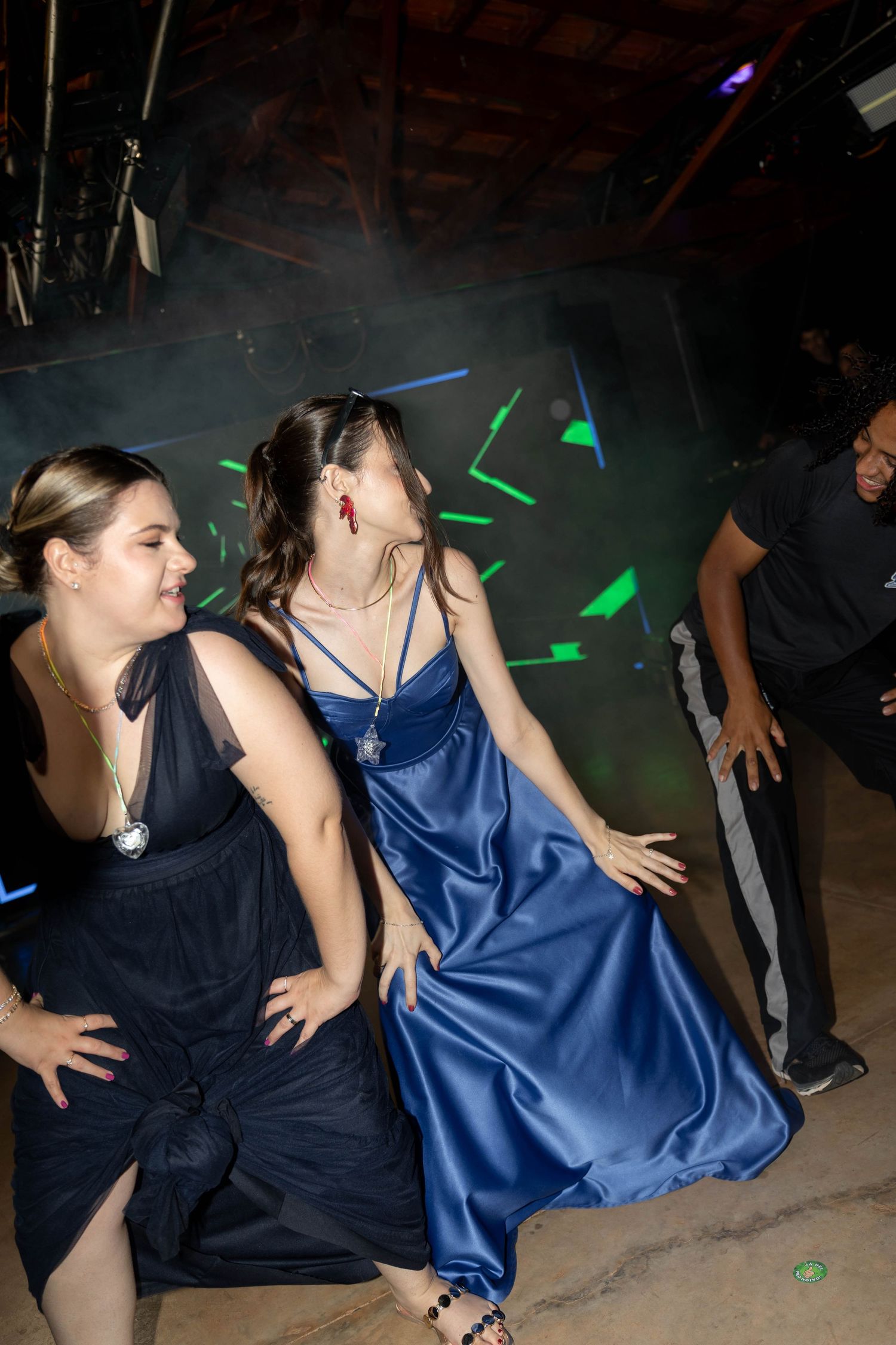 Two women in elegant blue gowns dancing at a formal event with green laser lights in the background.